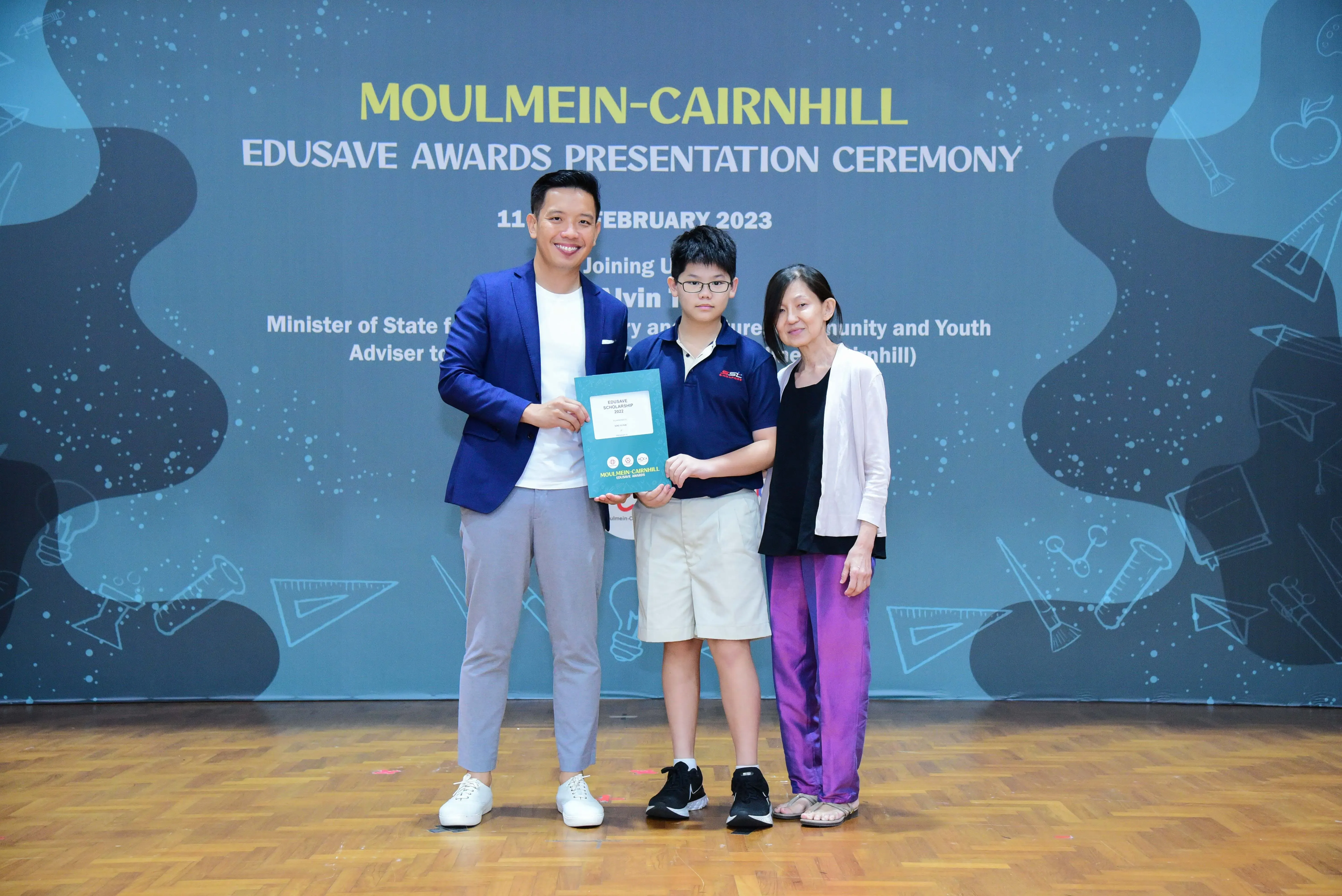 Three people pose on a stage at the Moulmein-Cairnhill Edusave Awards Presentation Ceremony, February 2023.