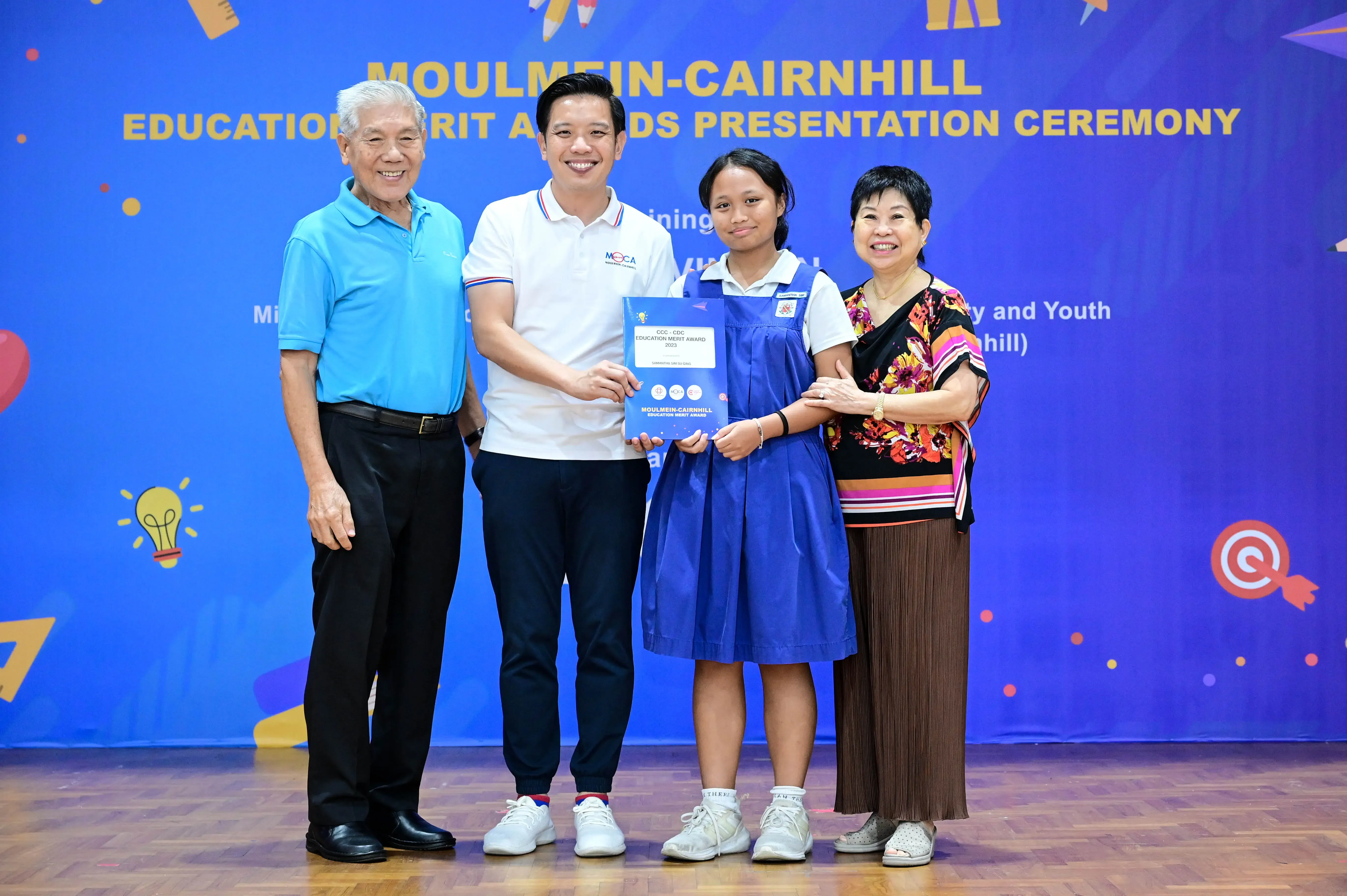 Four people smile while holding an award certificate at the Moulmein-Cairnhill Education Merit Awards Presentation Ceremony.