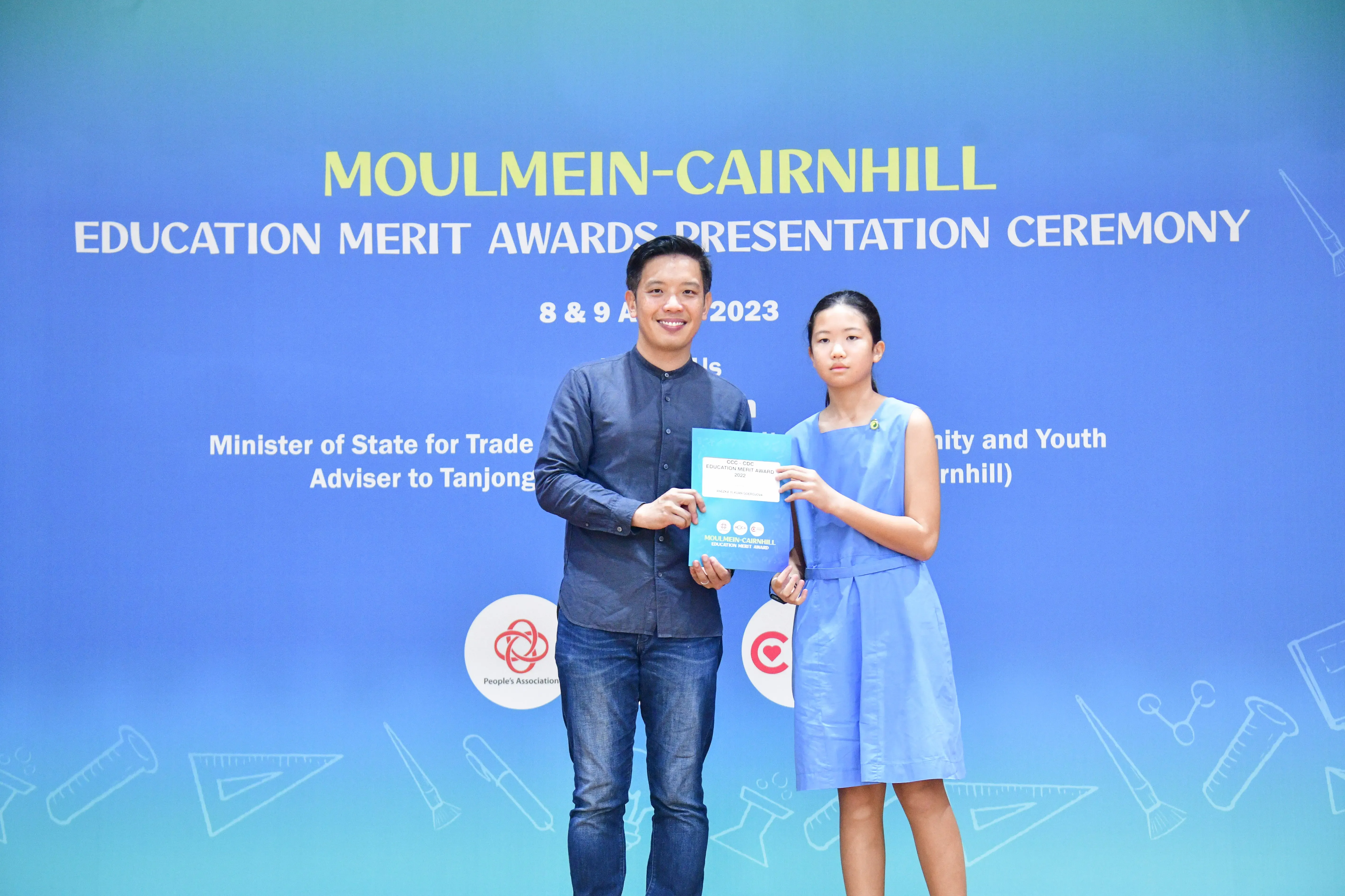 A man and a girl hold an award booklet at the Moulmein-Cairnhill Education Merit Awards Ceremony 2023.