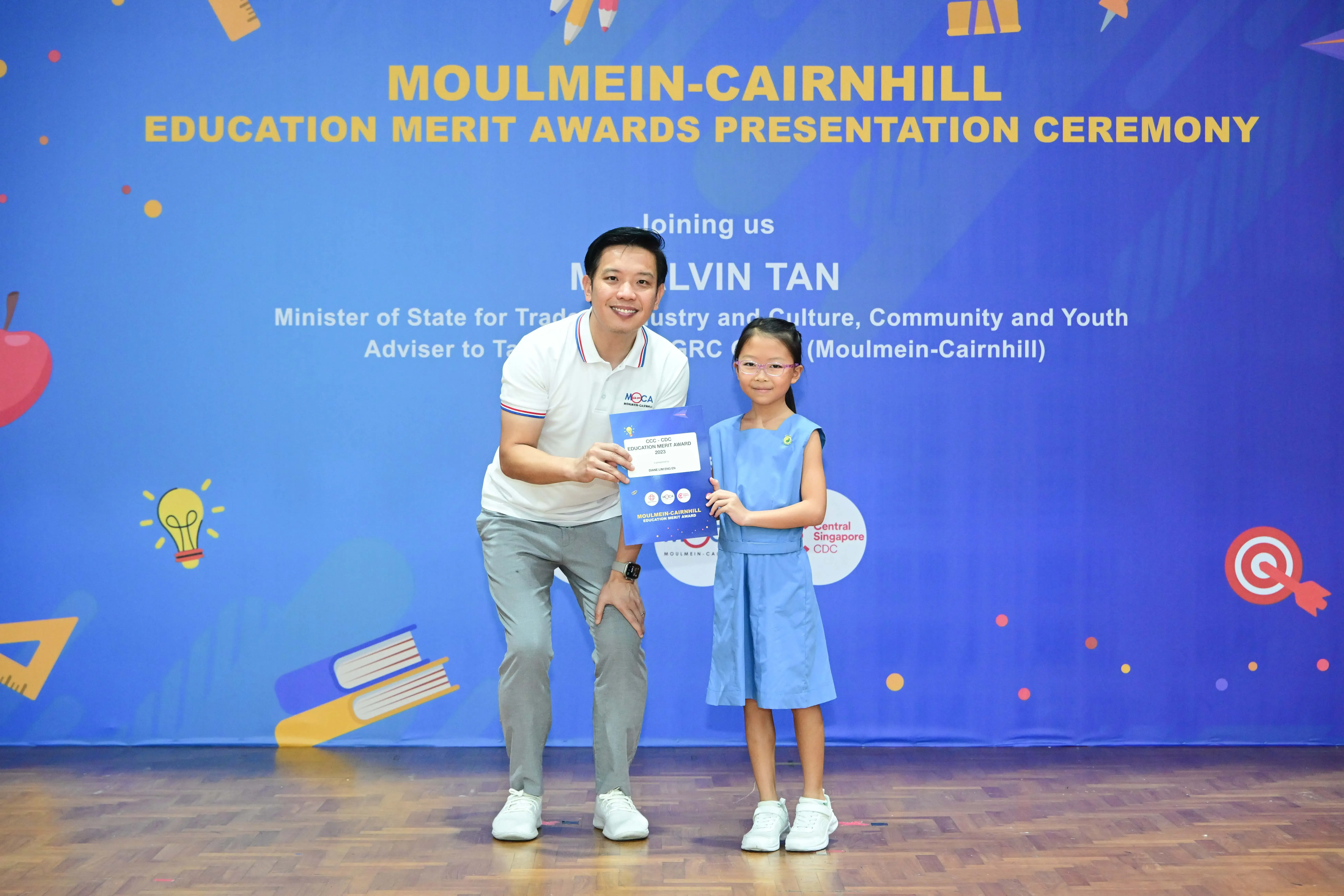 A man and a young girl hold a certificate at the Moulmein-Cairnhill Education Merit Awards Presentation Ceremony.