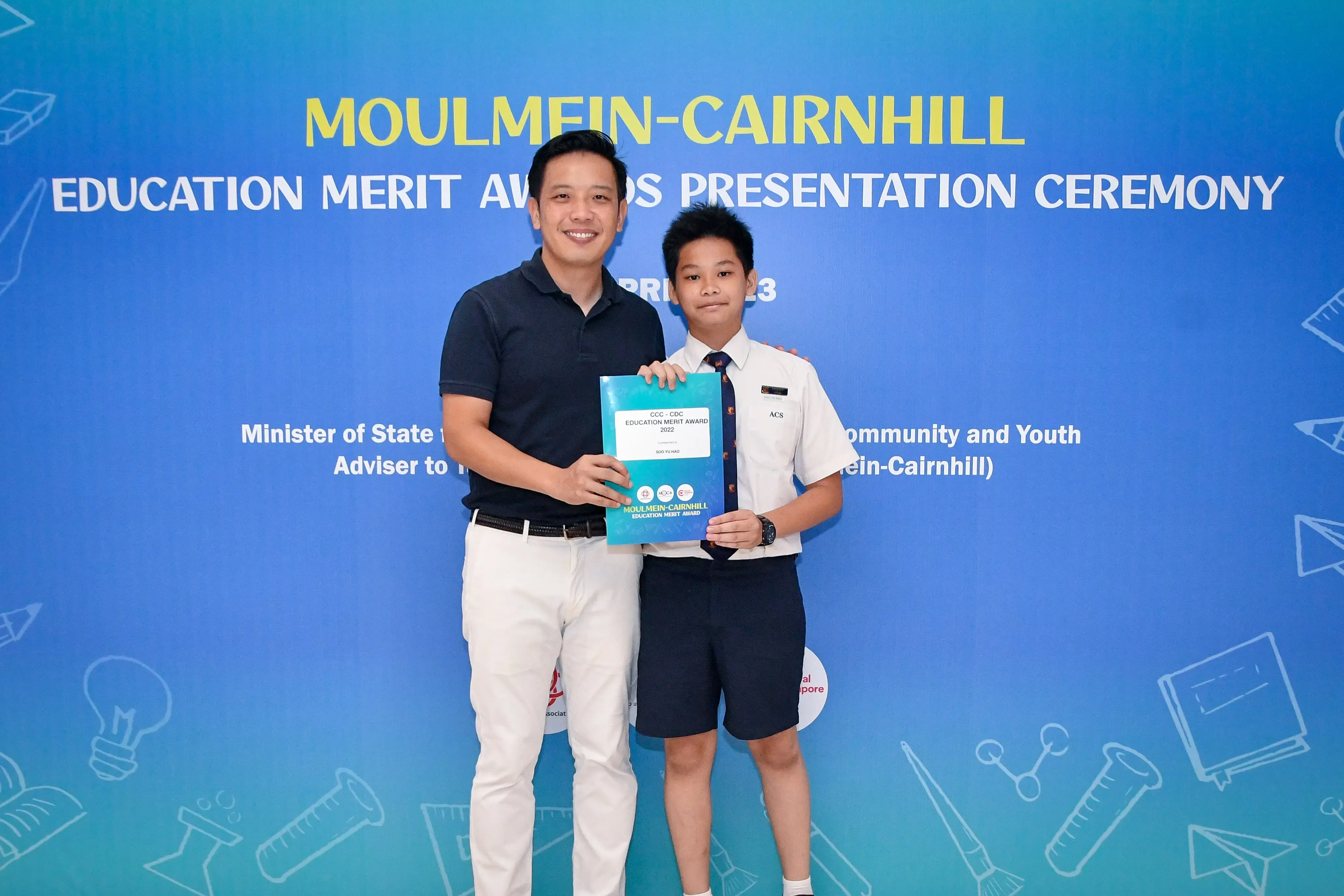 Adult and young student holding an award certificate at Moulmein-Cairnhill Education Merit Awards Presentation Ceremony.