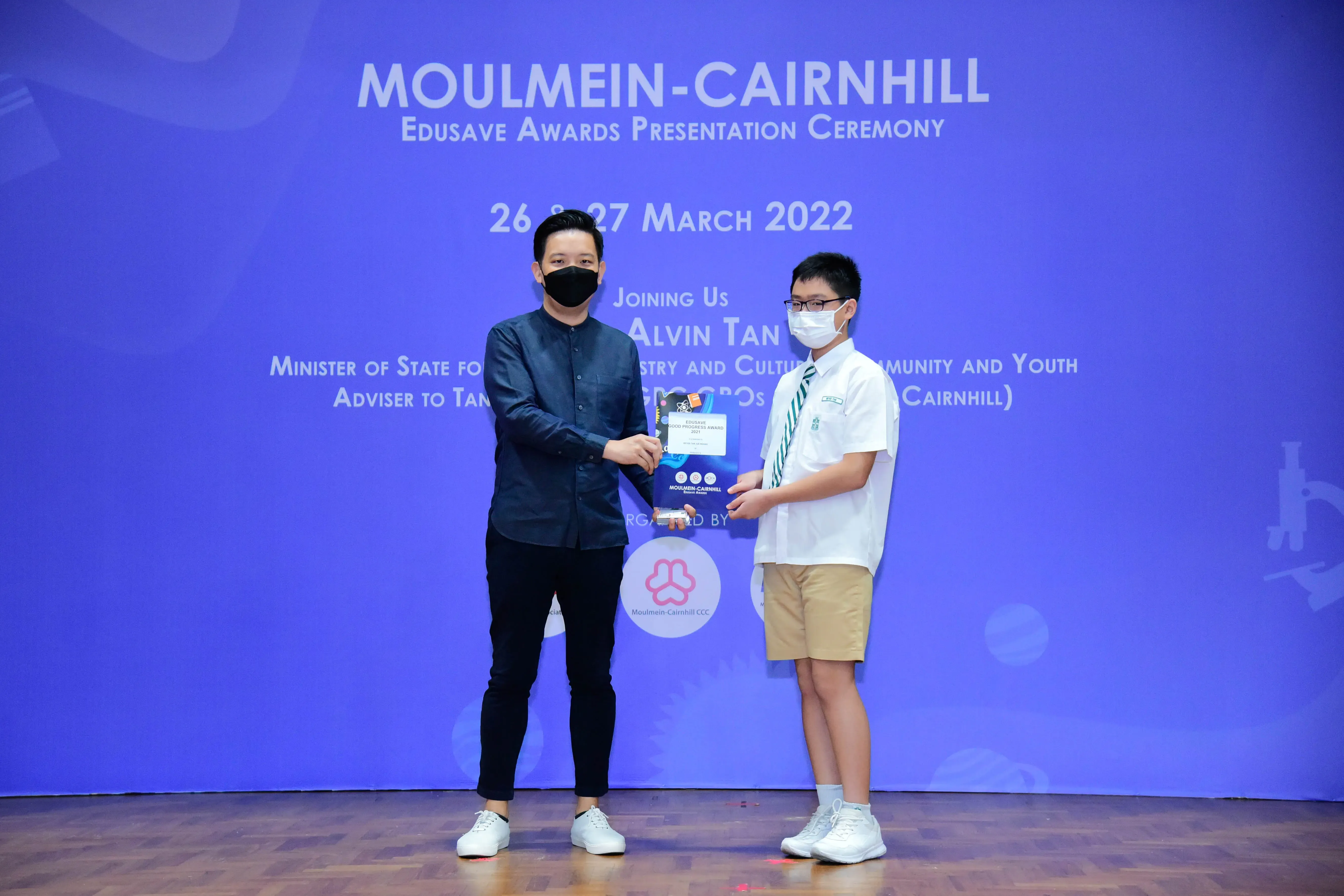 An adult and a uniformed student exchange an award on stage at the Moulmein-Cairnhill Edusave Awards Ceremony, March 2022.