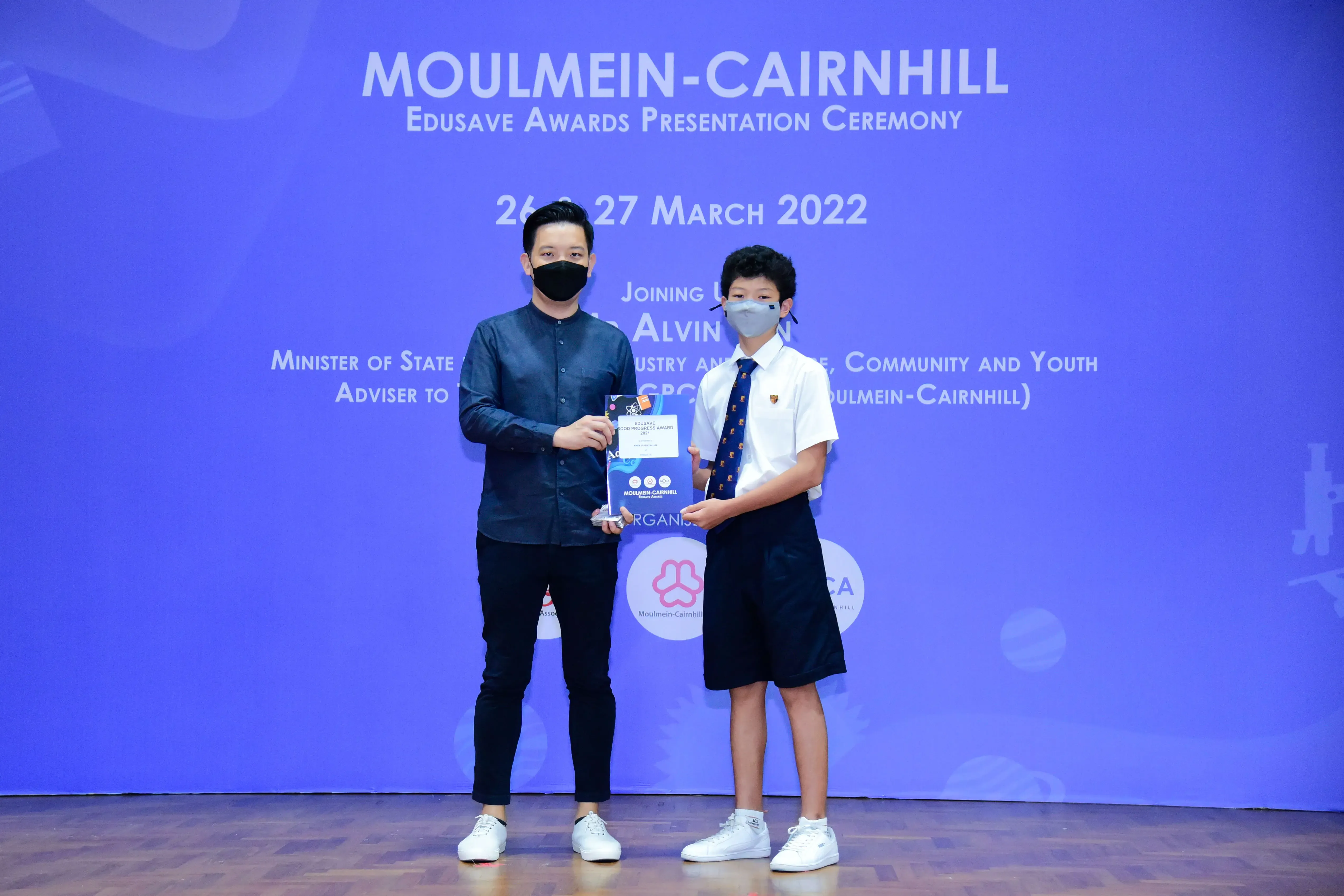 An adult and a young student in uniform hold an award together at the Moulmein-Cairnhill Edusave Awards Ceremony 2022.