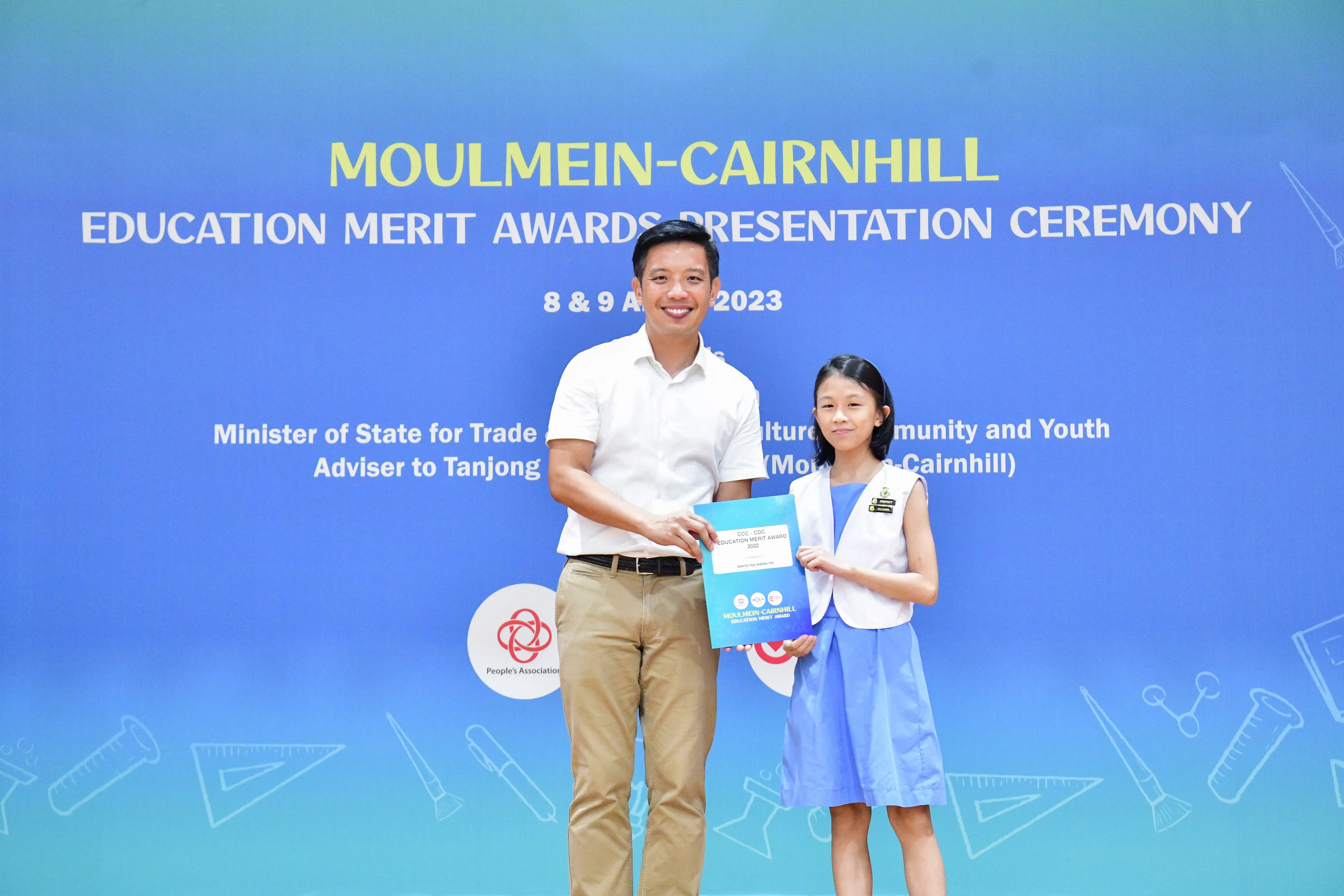 A man and a young girl hold an award certificate at the Moulmein-Cairnhill Education Merit Awards Ceremony 2023.