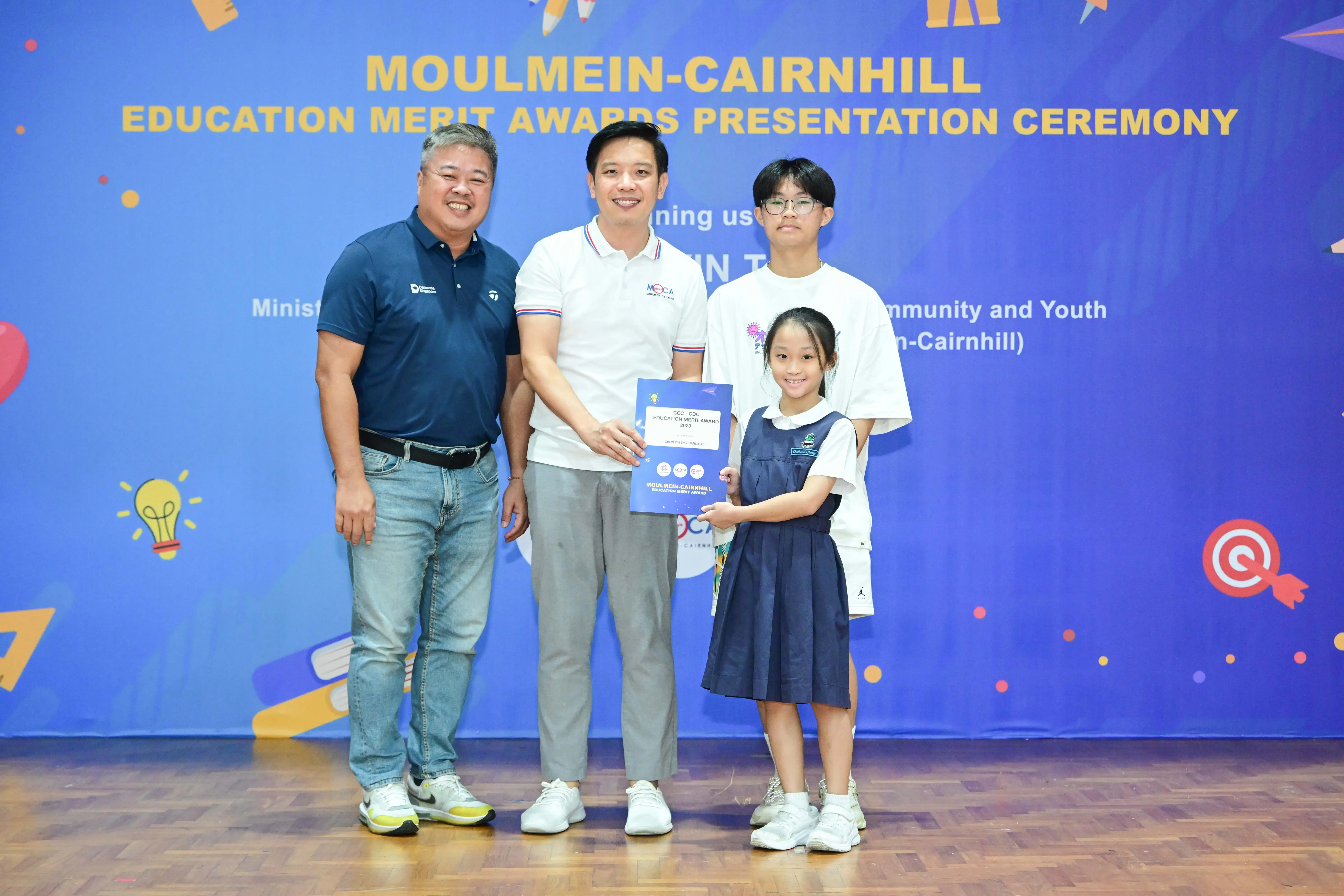 Two men and two children pose holding a certificate at the Moulmein-Cairnhill Education Merit Awards Ceremony.