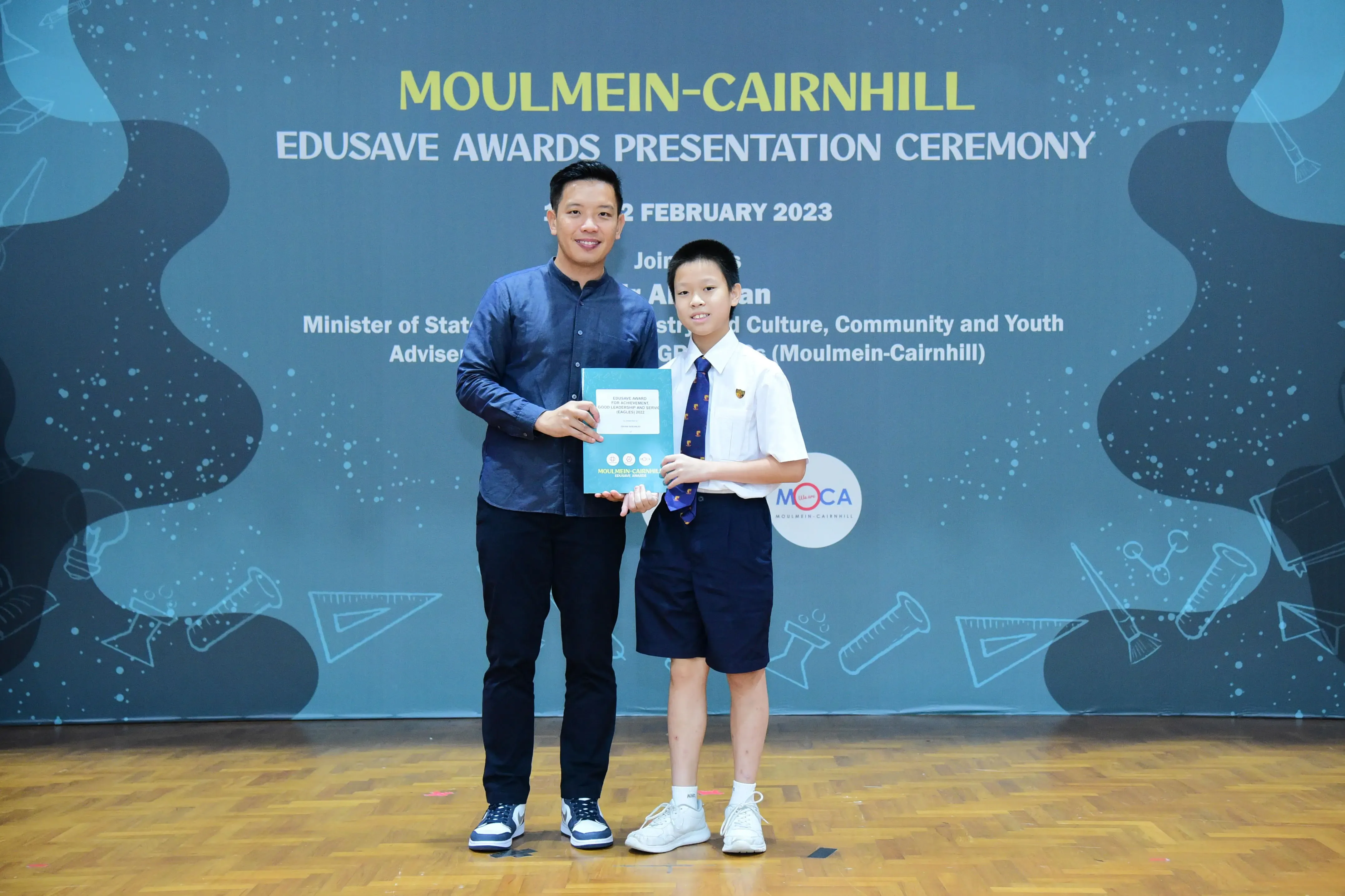 An adult and a uniformed student hold an award together at the Moulmein-Cairnhill Edusave Awards Ceremony 2023.