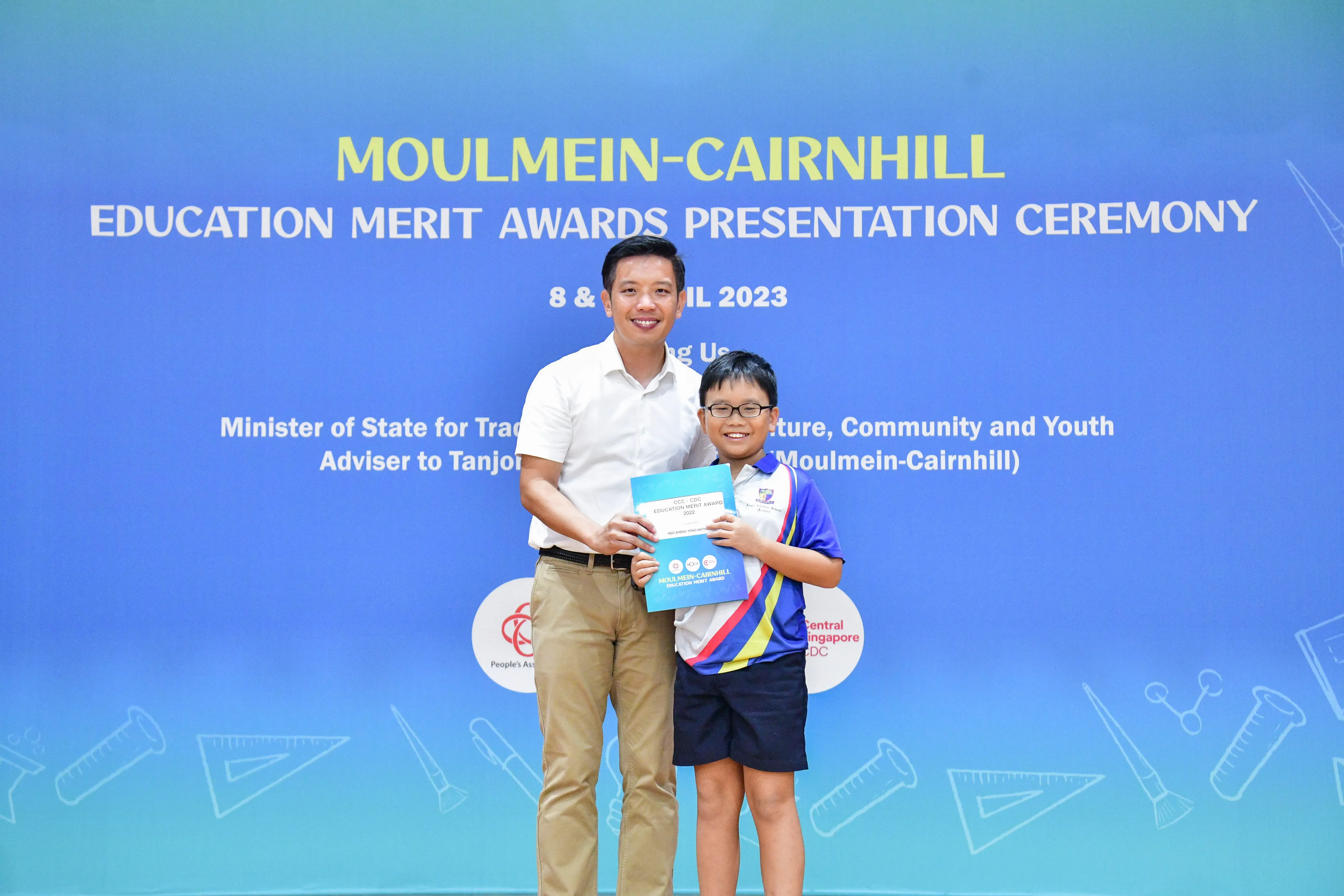 A man and a young boy hold a certificate together at the Moulmein-Cairnhill Education Merit Awards Ceremony 2023.