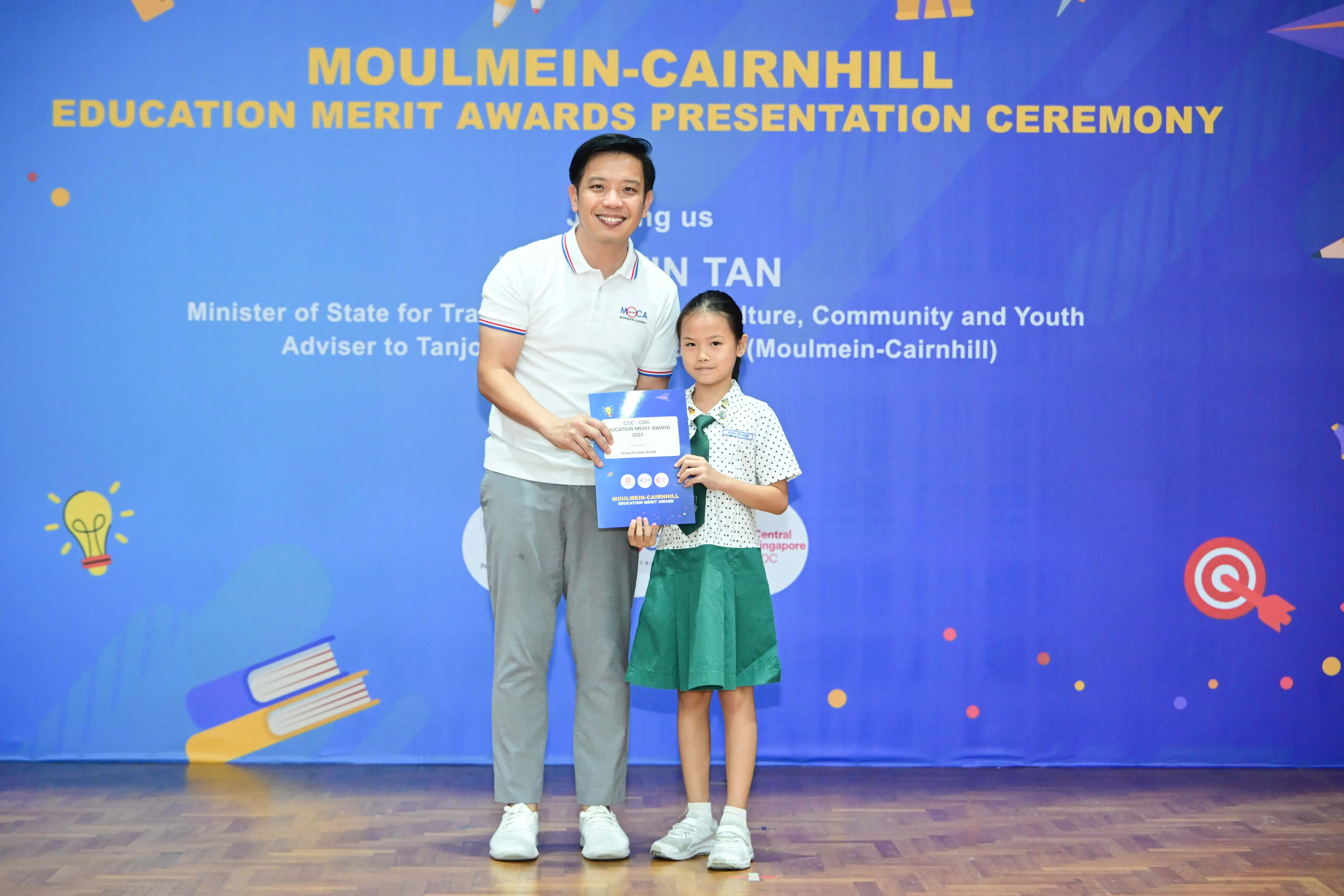Man and young girl hold a certificate at the Moulmein-Cairnhill Education Merit Awards Presentation Ceremony.