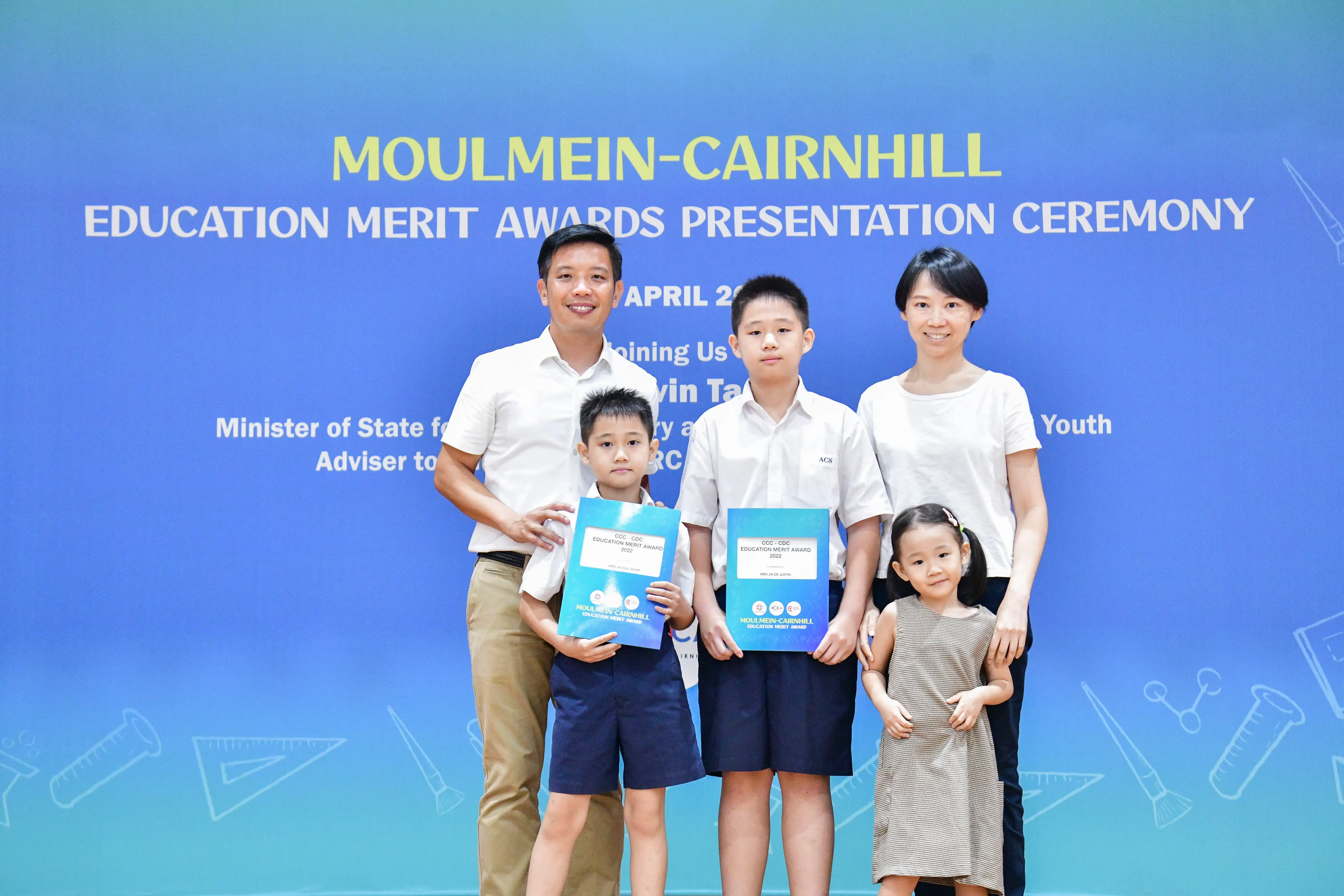 Family of five posing at the Moulmein-Cairnhill Education Merit Awards Presentation Ceremony, two boys holding award folders.