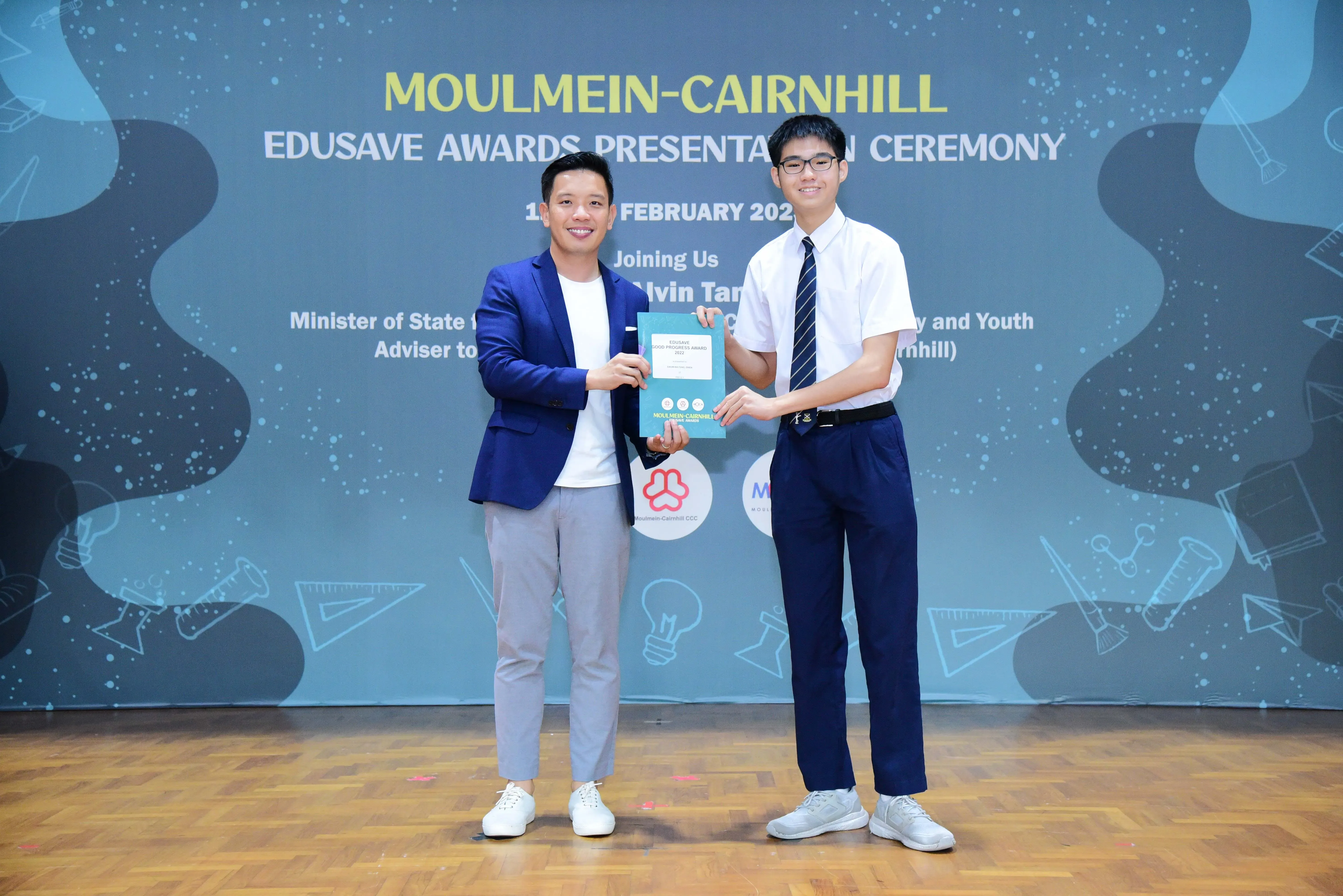 Two men smile while holding an award folder at the Moulmein-Cairnhill Edusave Awards Presentation Ceremony.
