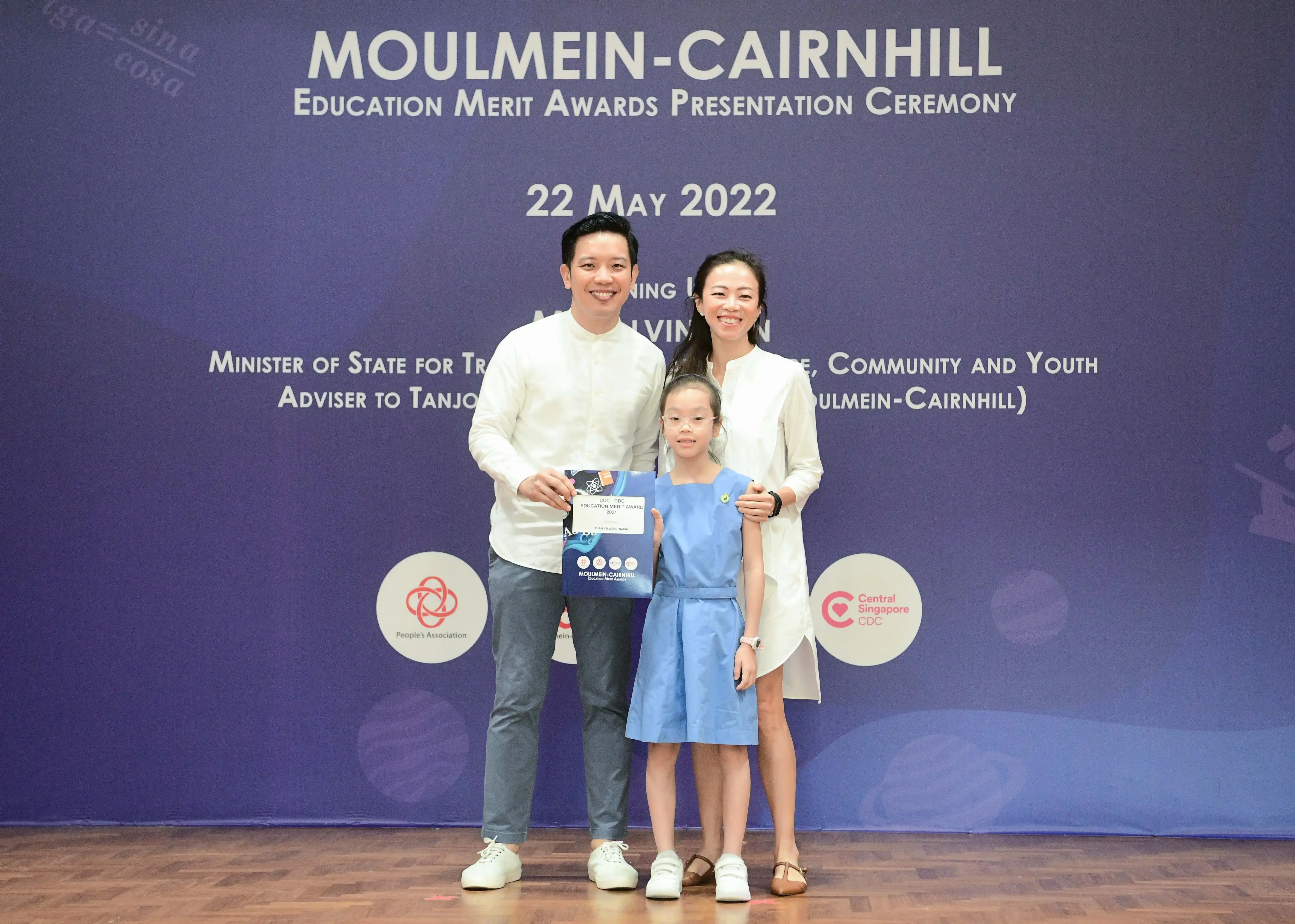 Two adults and a young girl pose with an award certificate at the Moulmein-Cairnhill Education Merit Awards ceremony, 22 May 2022.