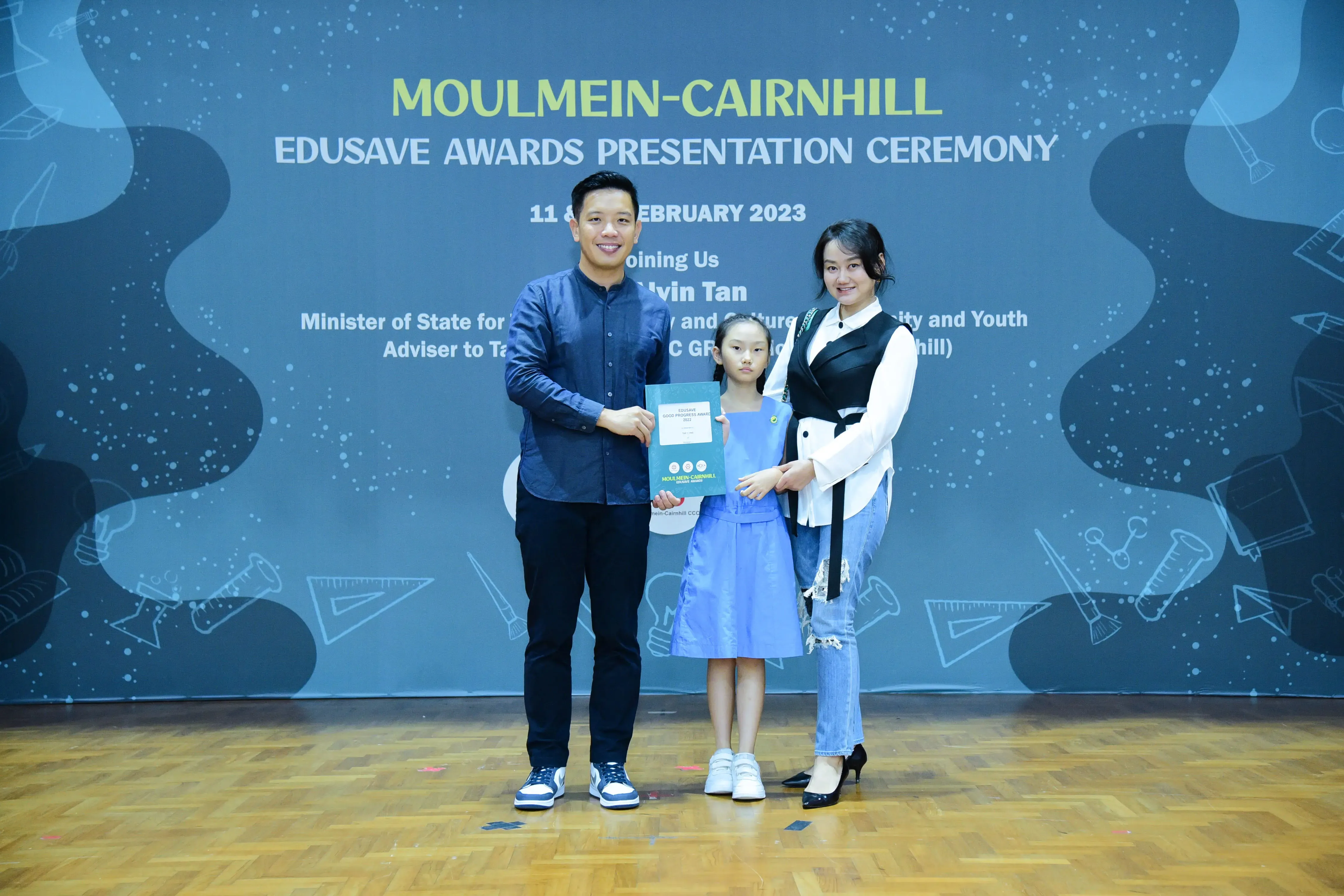 A man and woman pose with a young girl holding a certificate at the Moulmein-Cairnhill Edusave Awards Ceremony 2023.