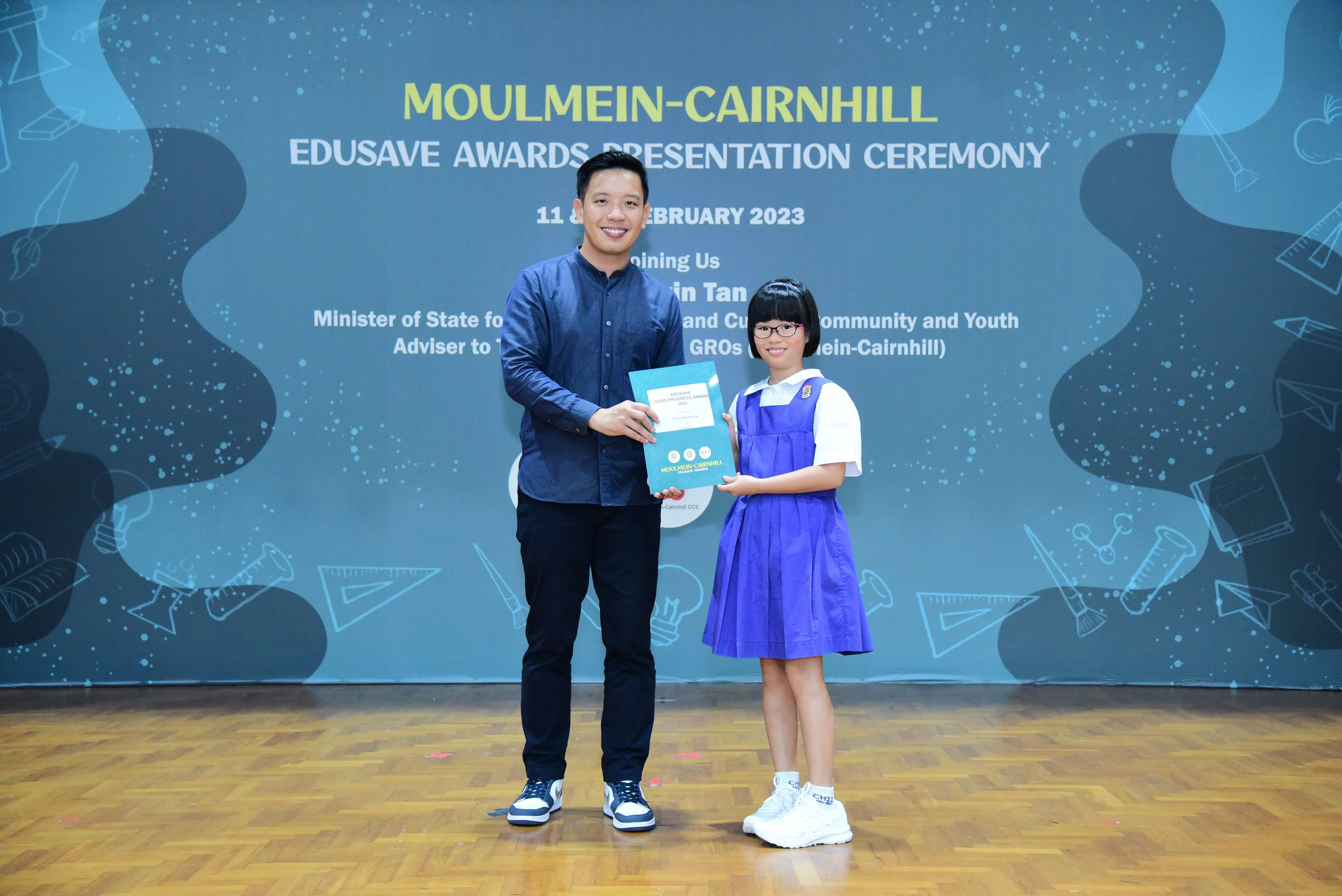 A man and a girl in school uniform hold an award certificate at the Moulmein-Cairnhill Edusave Awards Ceremony 2023.