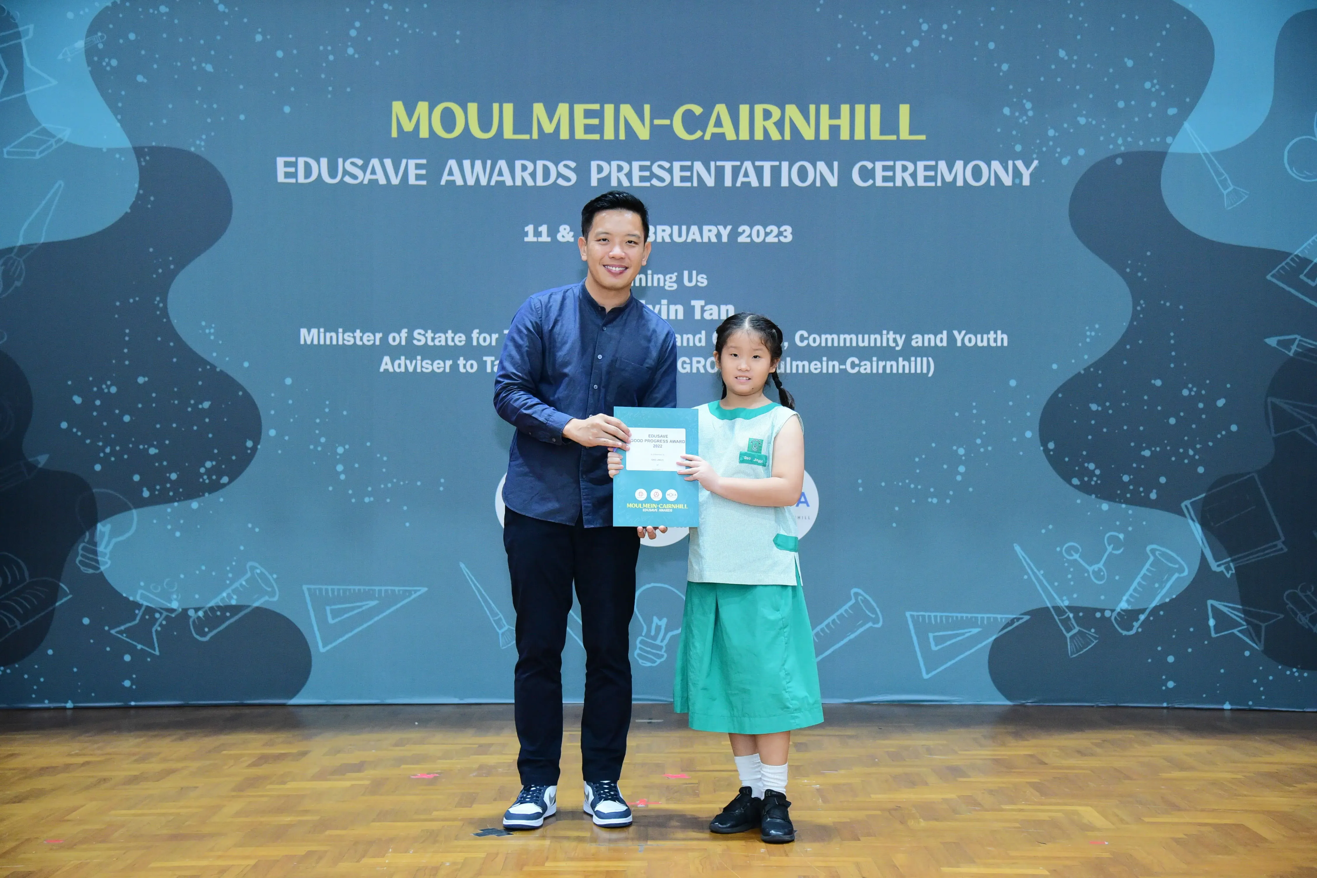 A man and a young girl hold a certificate at the Moulmein-Cairnhill Edusave Awards Ceremony, February 2023.