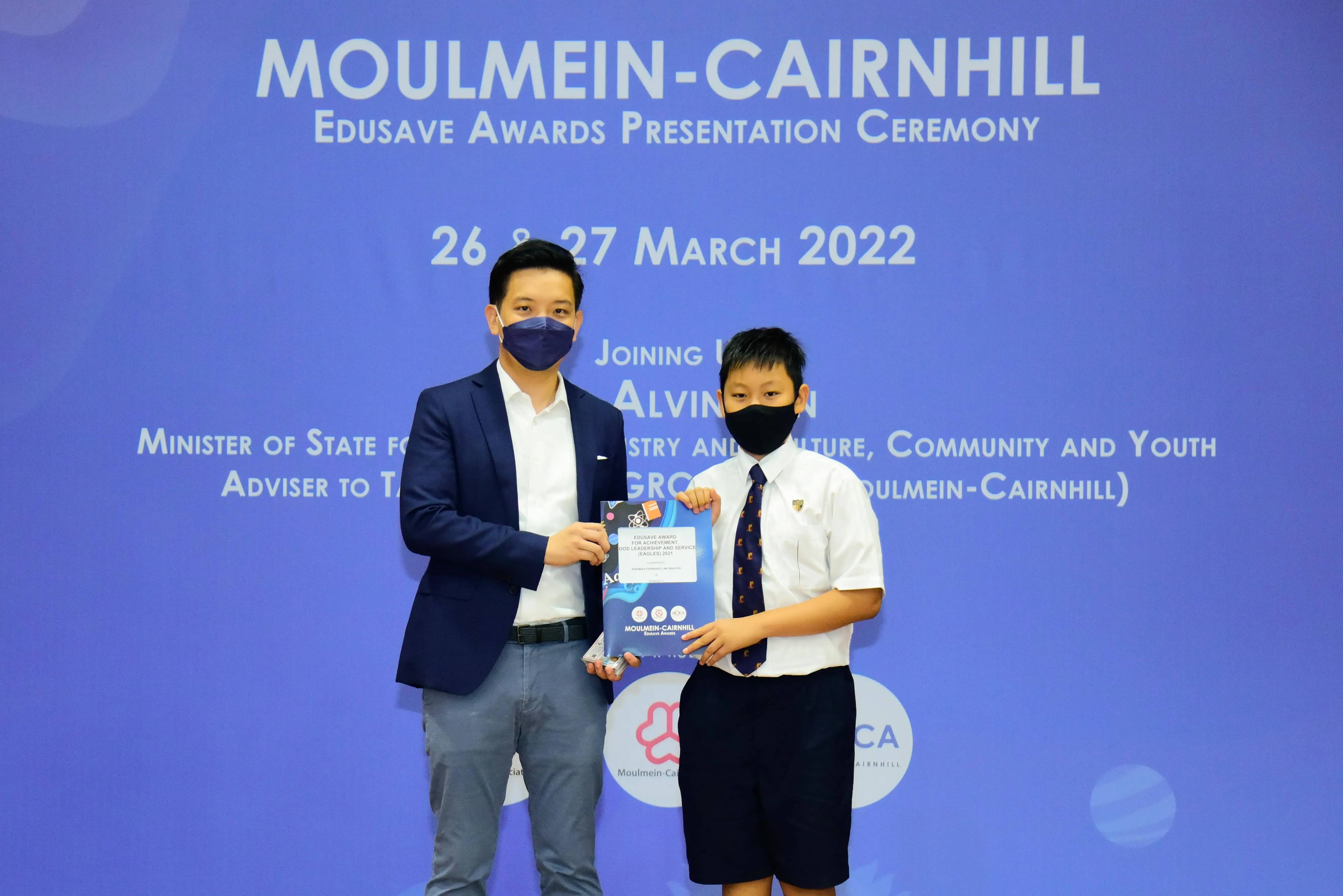 An adult and a school student in masks hold an award at the Moulmein-Cairnhill Edusave Awards Ceremony, March 2022.