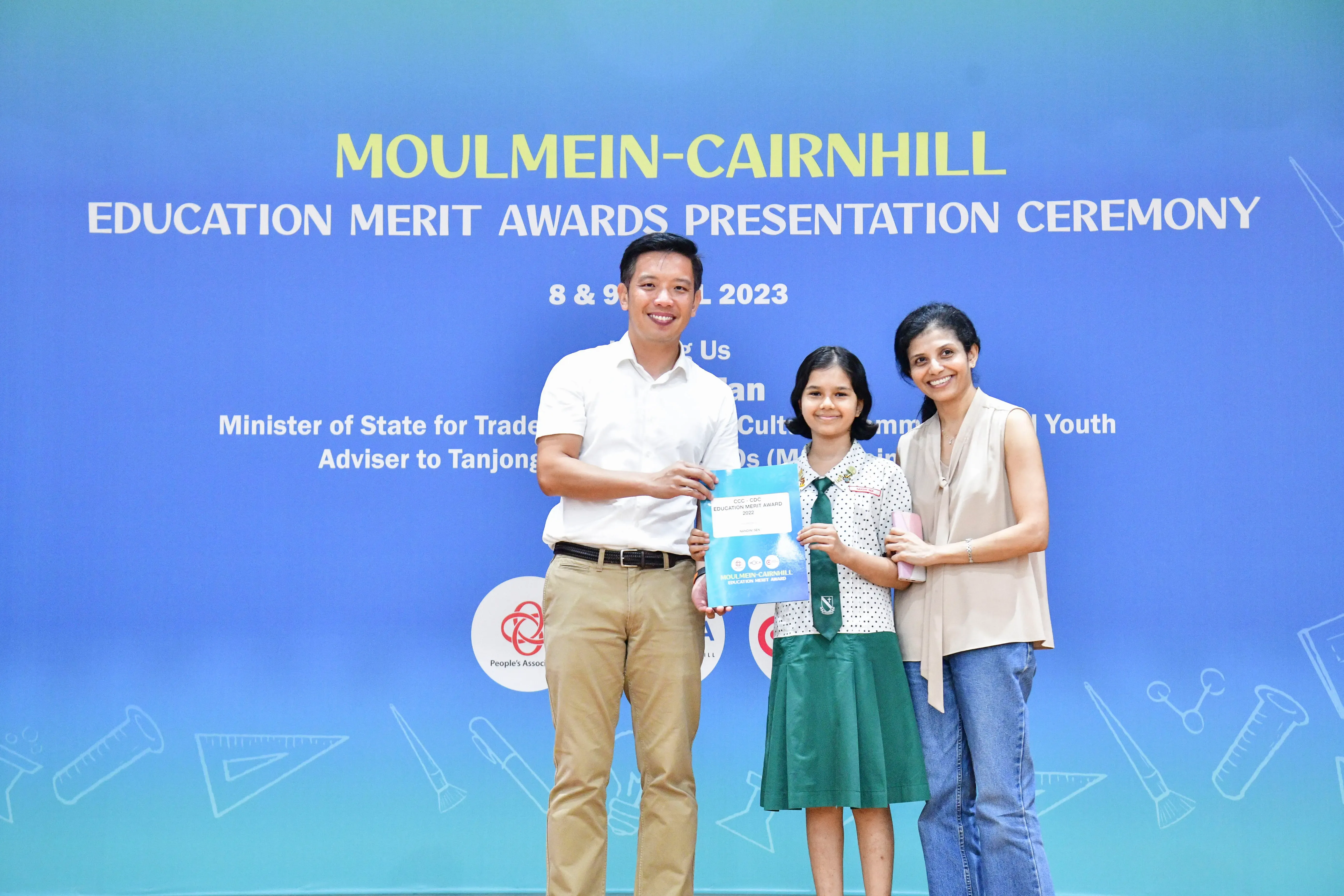 A girl in school uniform holds an award certificate flanked by two adults at the Moulmein-Cairnhill Education Merit Awards 2023.