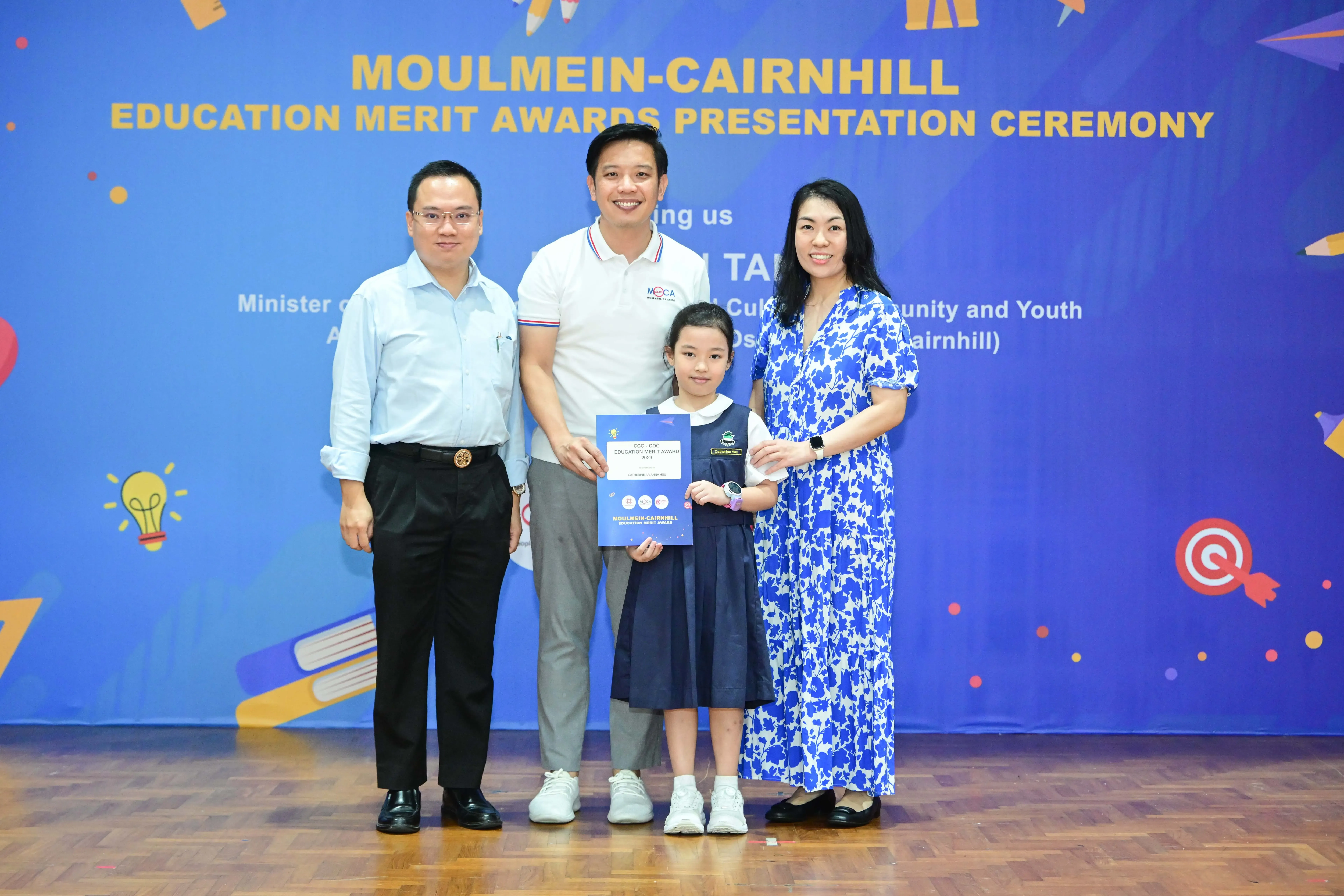 Three adults and a young girl pose at the Moulmein-Cairnhill Education Merit Awards Presentation Ceremony, girl holding a certificate.