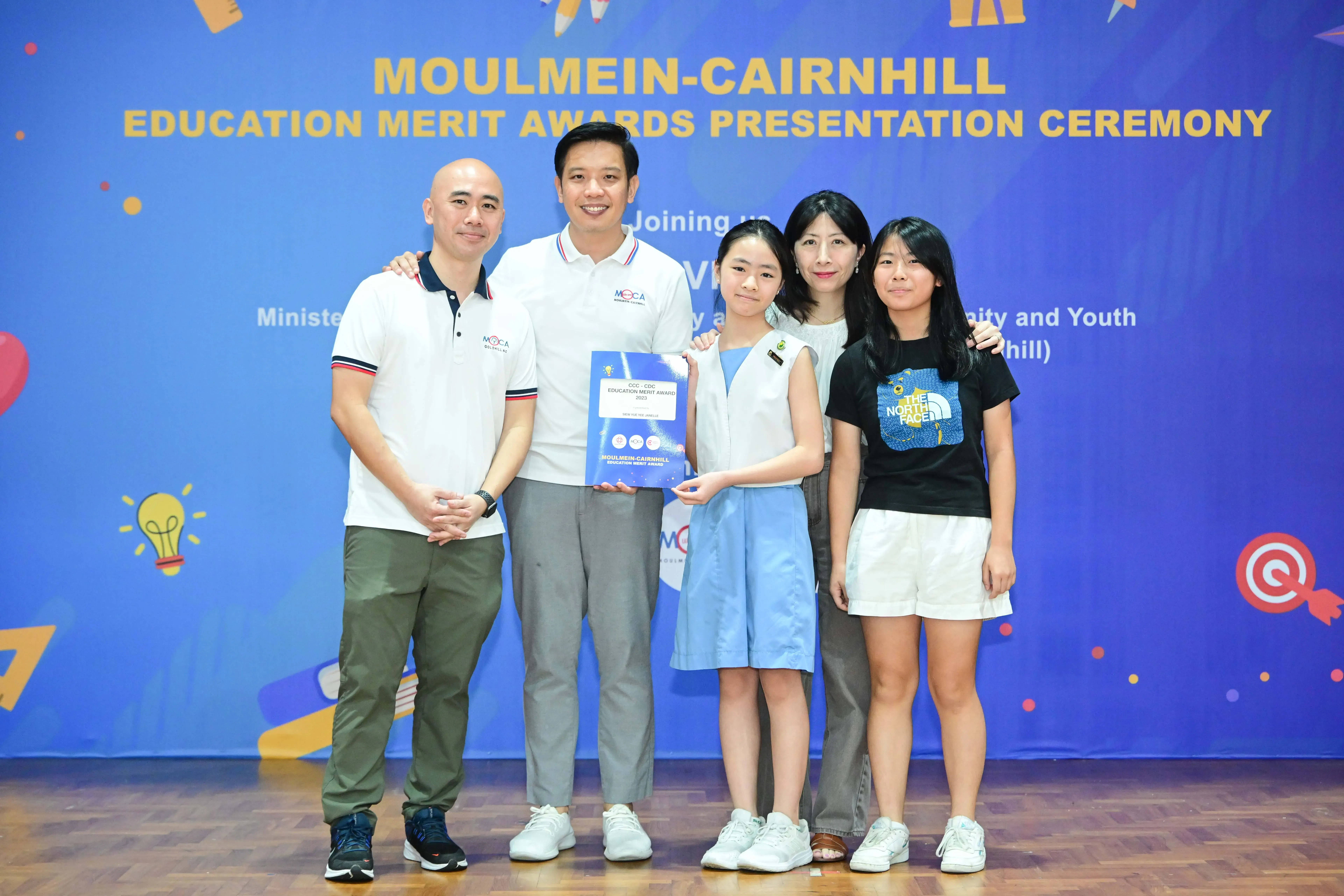 Five people pose together at the Moulmein-Cairnhill Education Merit Awards Presentation Ceremony, holding a certificate.