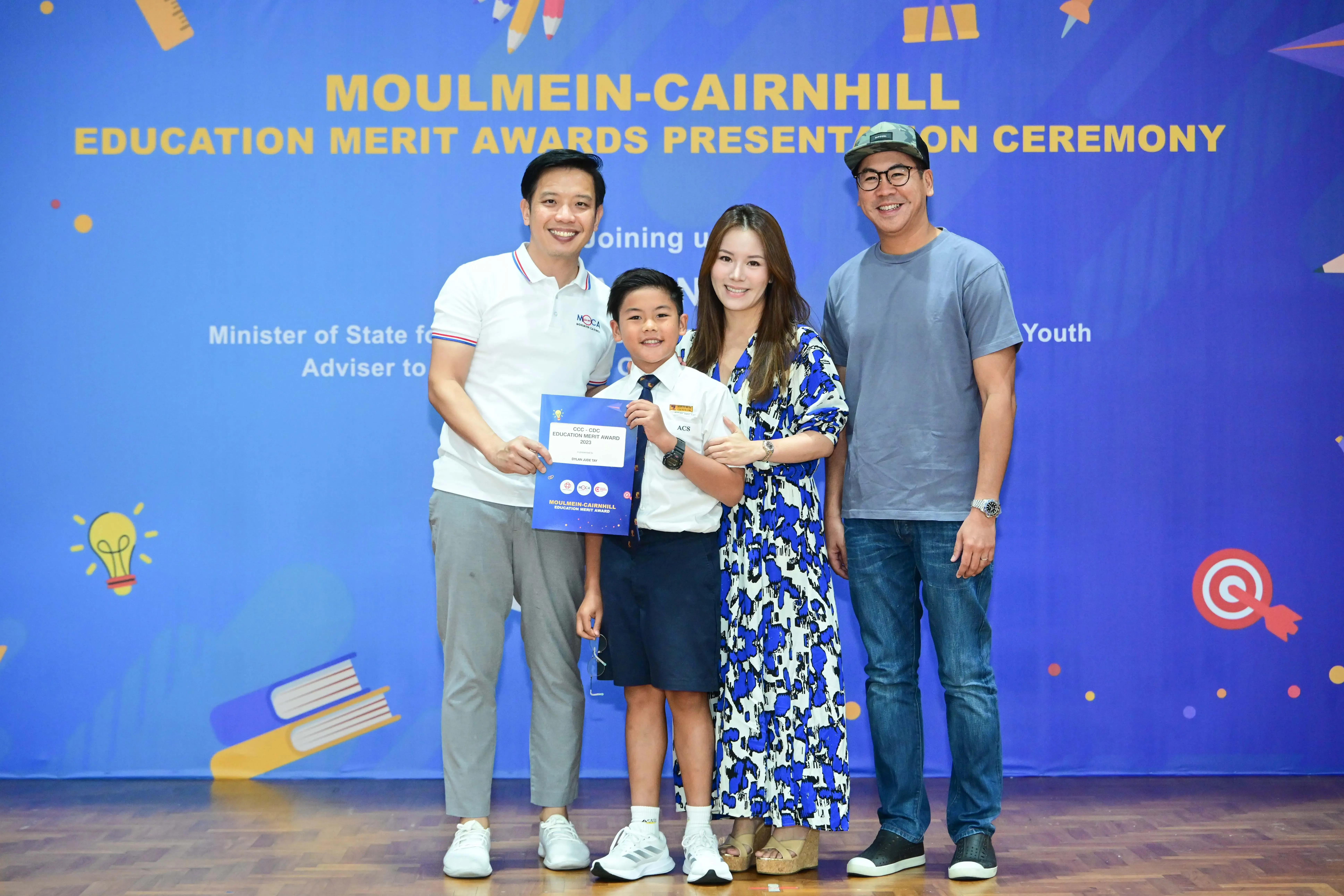 Four people pose at the Moulmein-Cairnhill Education Merit Awards, with a young boy holding a certificate.