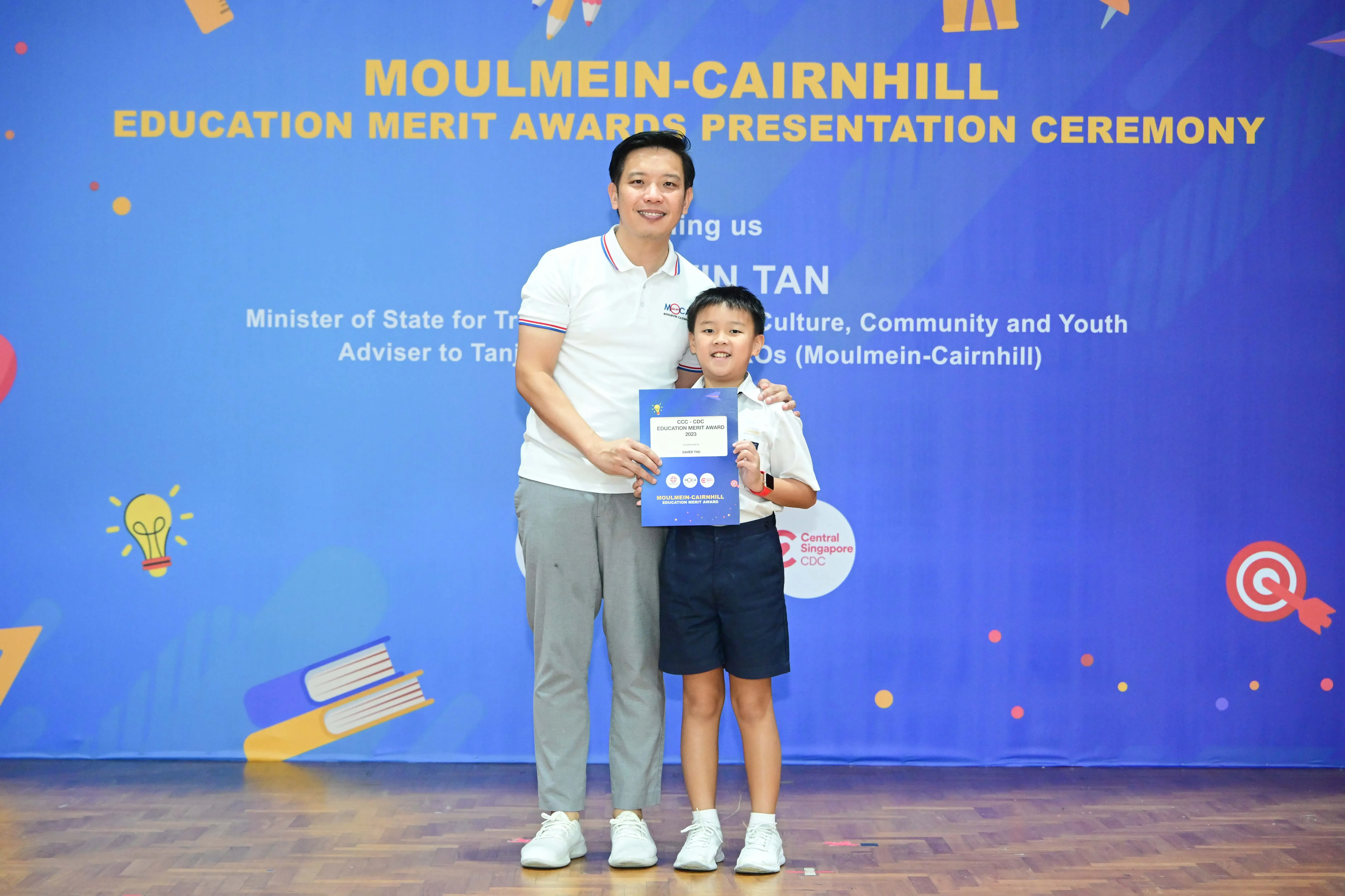 A man and a young boy pose together holding a certificate at the Moulmein-Cairnhill Education Merit Awards ceremony.