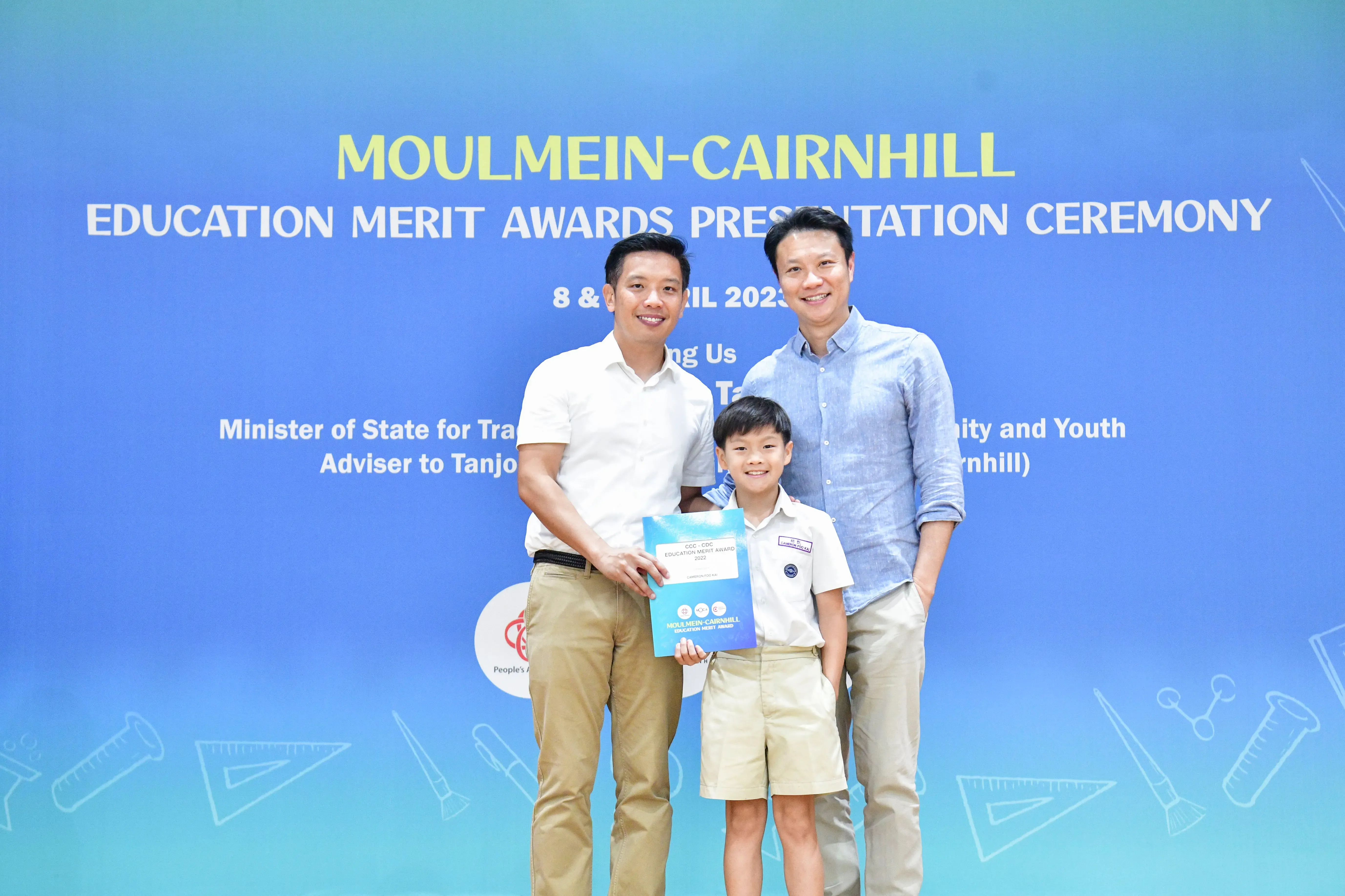 Two men and a young boy holding an award certificate pose at the Moulmein-Cairnhill Education Merit Awards ceremony.