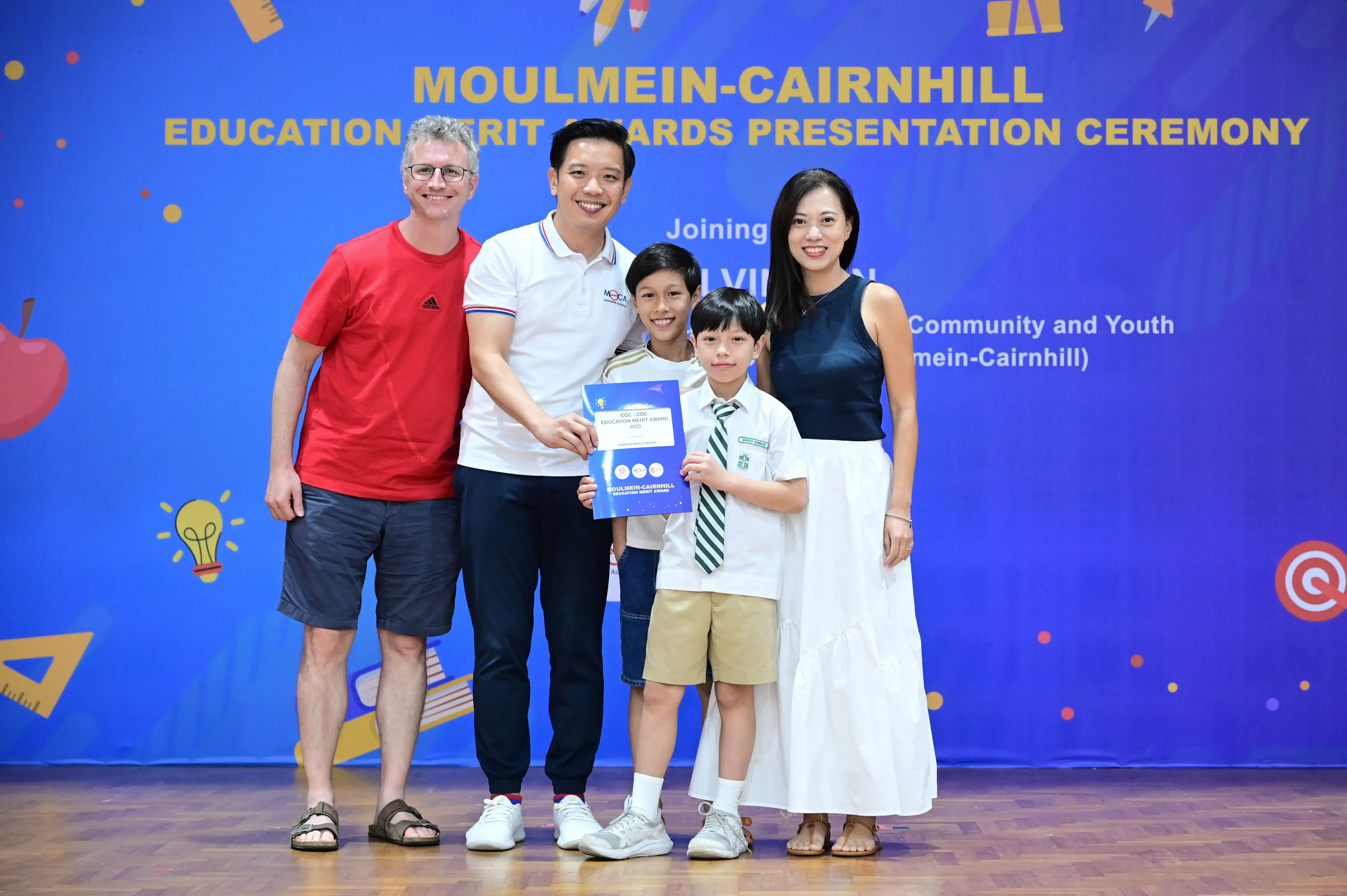 Two adults and two children pose with a certificate at the Moulmein-Cairnhill Education Merit Awards ceremony.