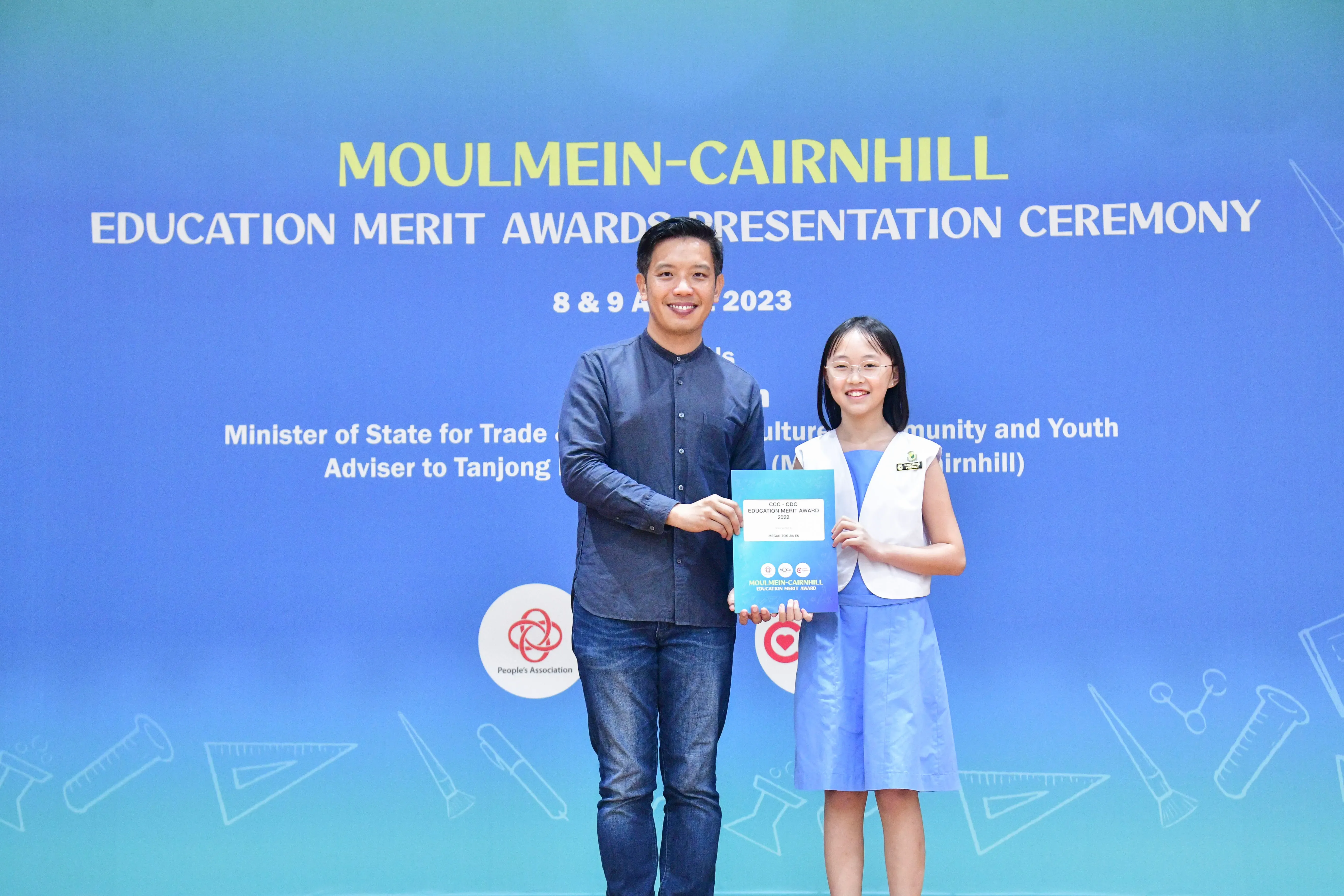 A man and a young girl hold an award certificate at the Moulmein-Cairnhill Education Merit Awards Ceremony 2023.