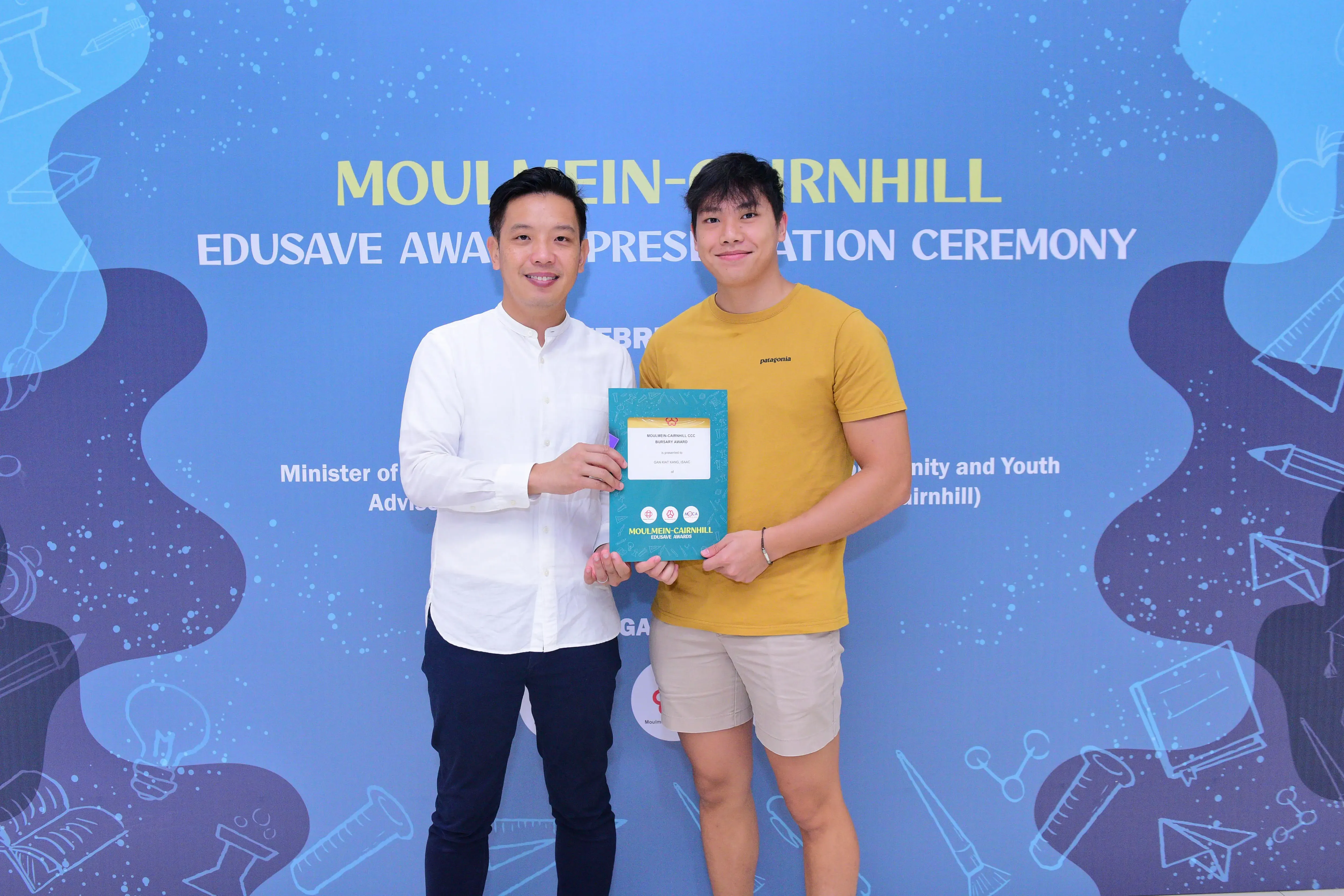 Two men smile while holding a certificate at the Moulmein-Cairnhill Edusave Award Presentation Ceremony.
