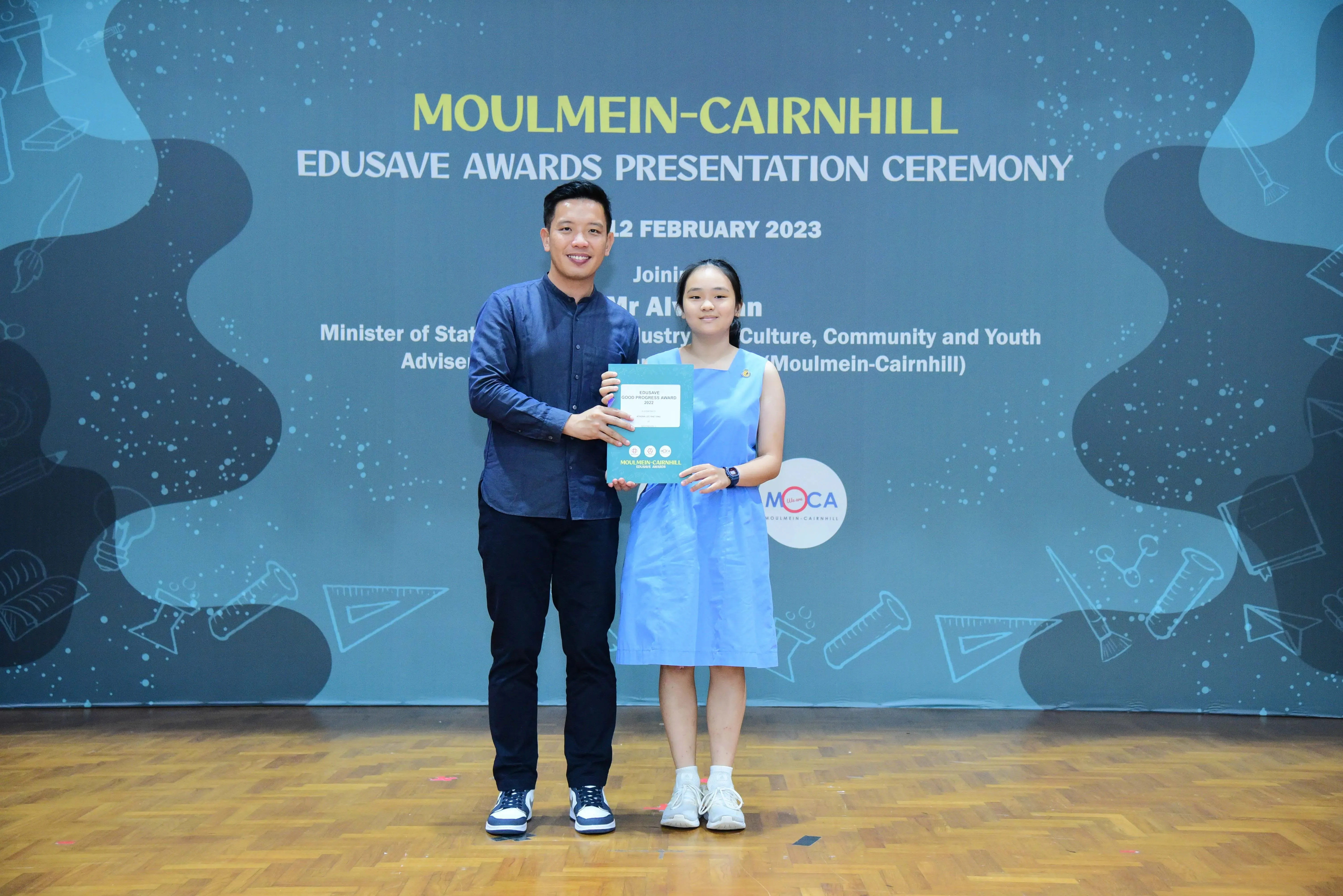 A man and a young girl hold a certificate together at the Moulmein-Cairnhill Edusave Awards Ceremony in February 2023.