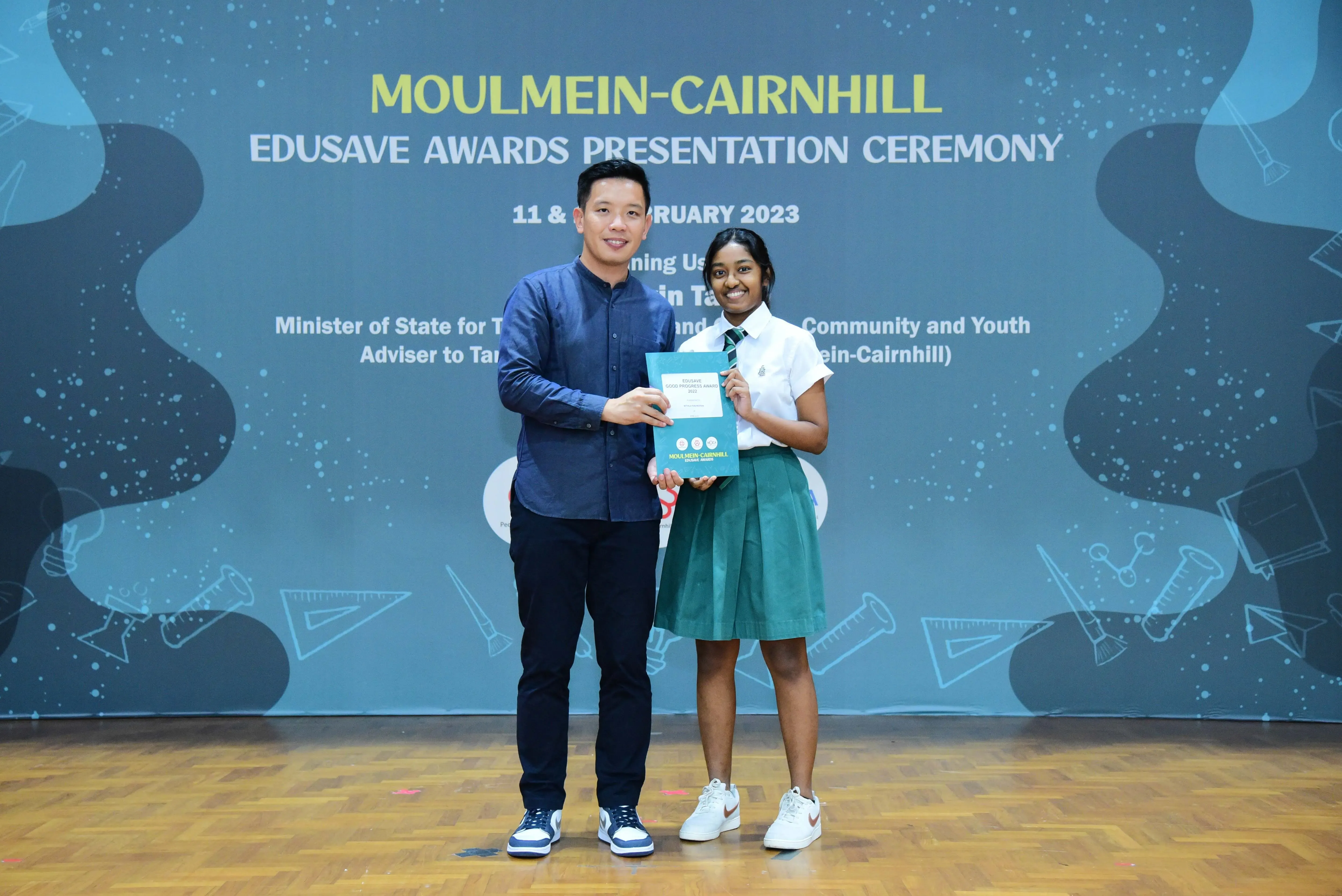 A man and a female student hold a certificate at the Moulmein-Cairnhill Edusave Awards Presentation Ceremony 2023.
