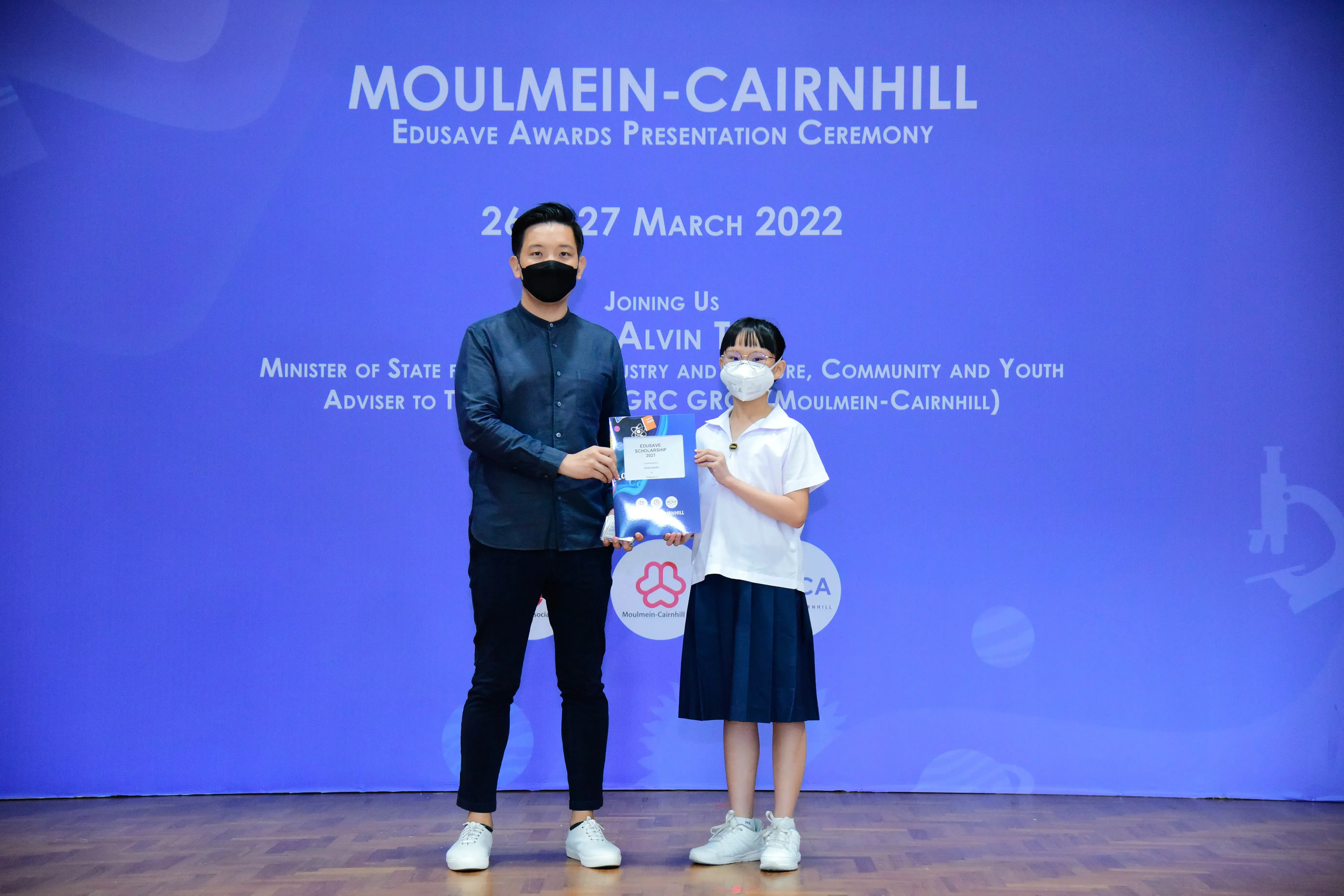 An adult and a student in uniform hold an award certificate at the Moulmein-Cairnhill Edusave Awards Ceremony 2022.