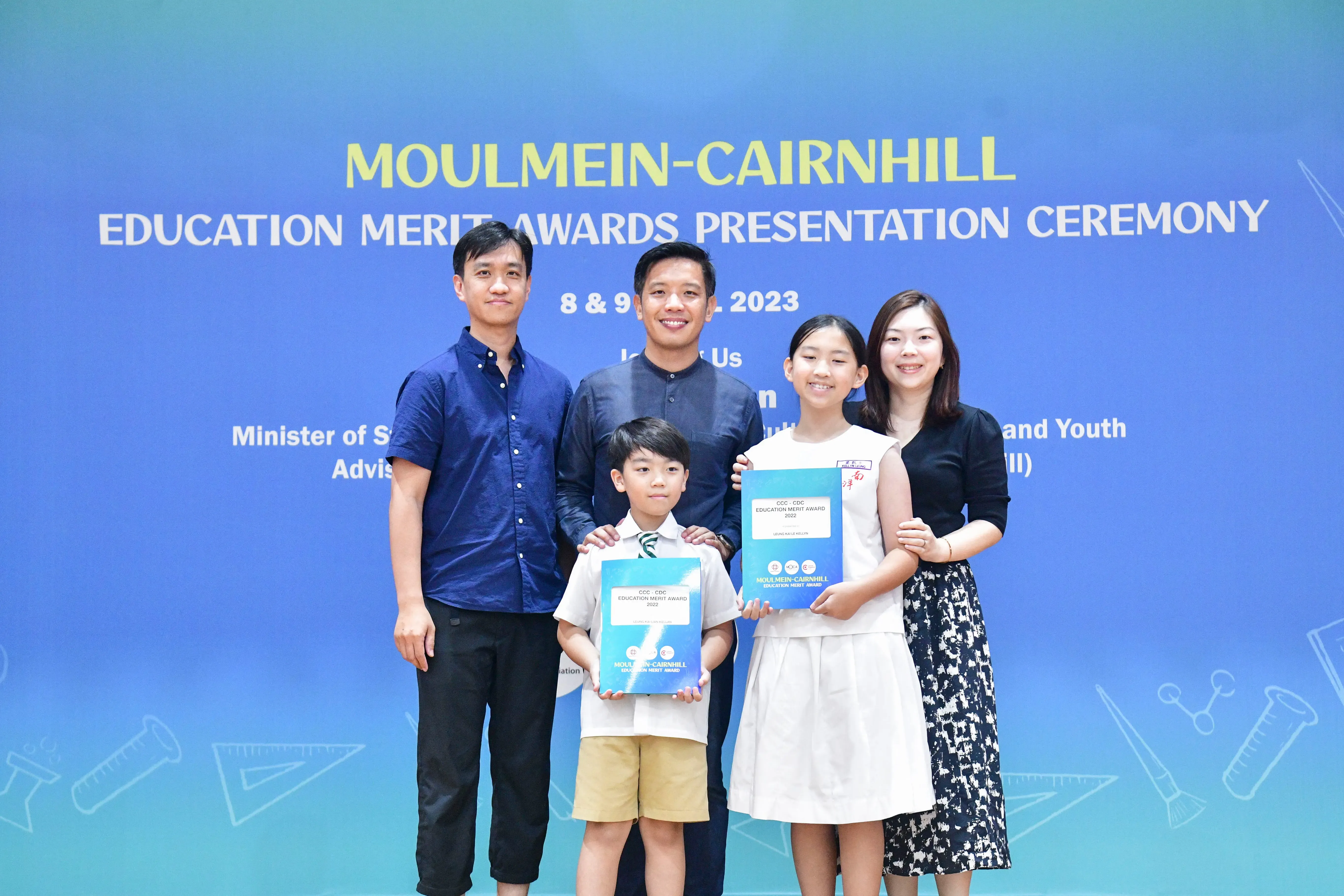 Five people pose at the Moulmein-Cairnhill Education Merit Awards Presentation Ceremony 2023, two children holding awards.