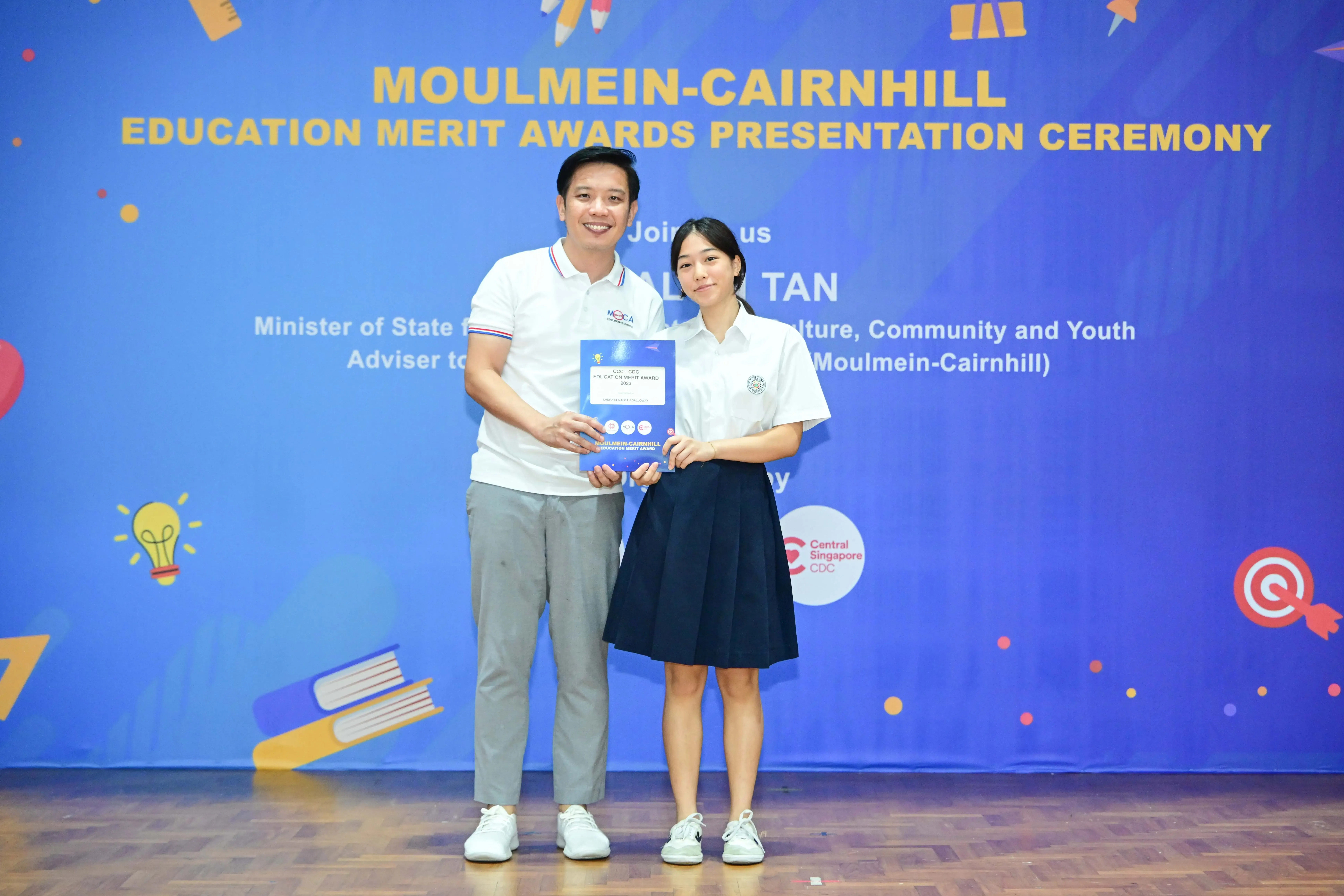 Two people hold a certificate together at the Moulmein-Cairnhill Education Merit Awards Presentation Ceremony.