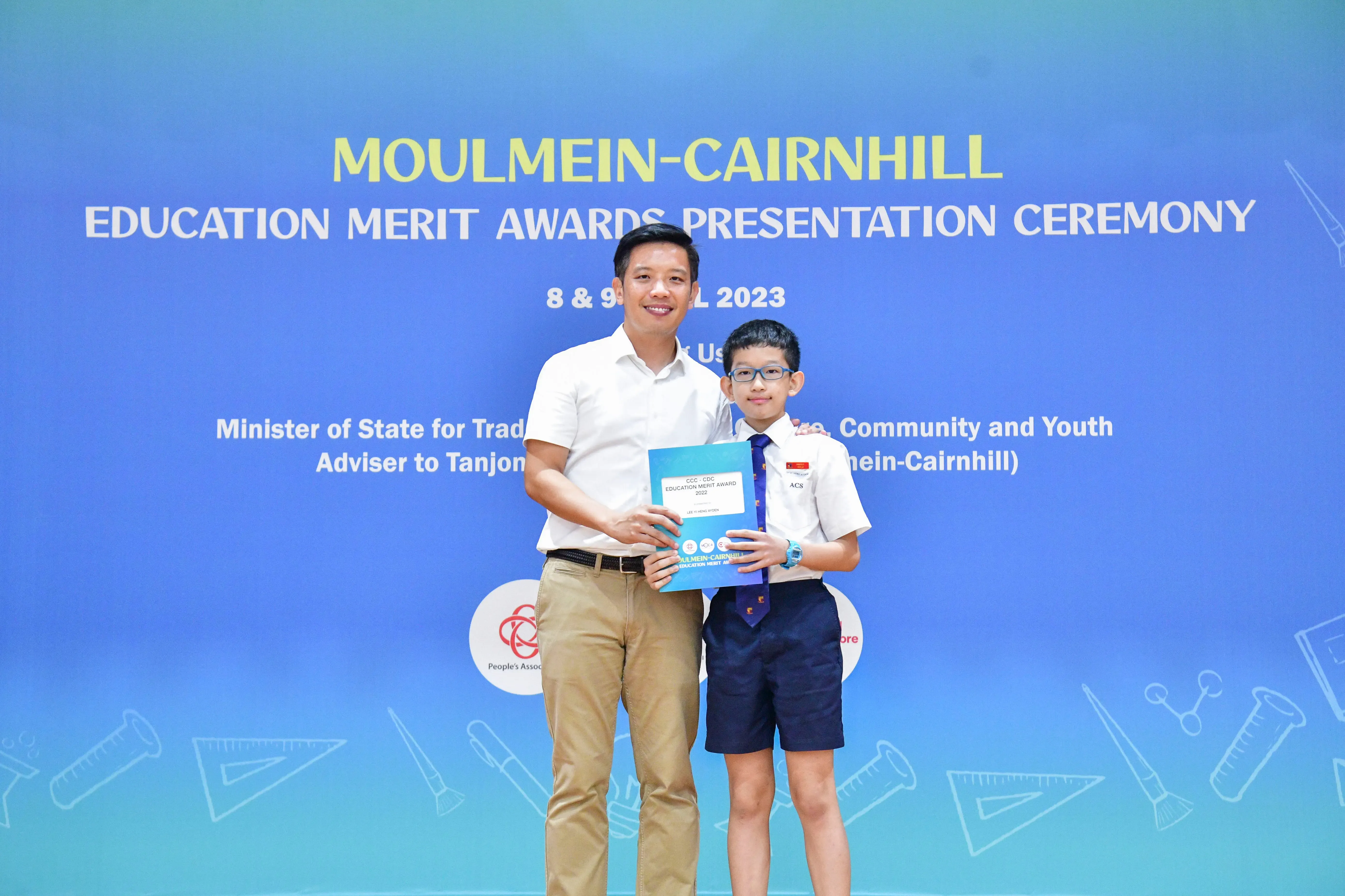 A man and a young boy in school uniform hold a certificate together at the Moulmein-Cairnhill Education Merit Awards 2023.