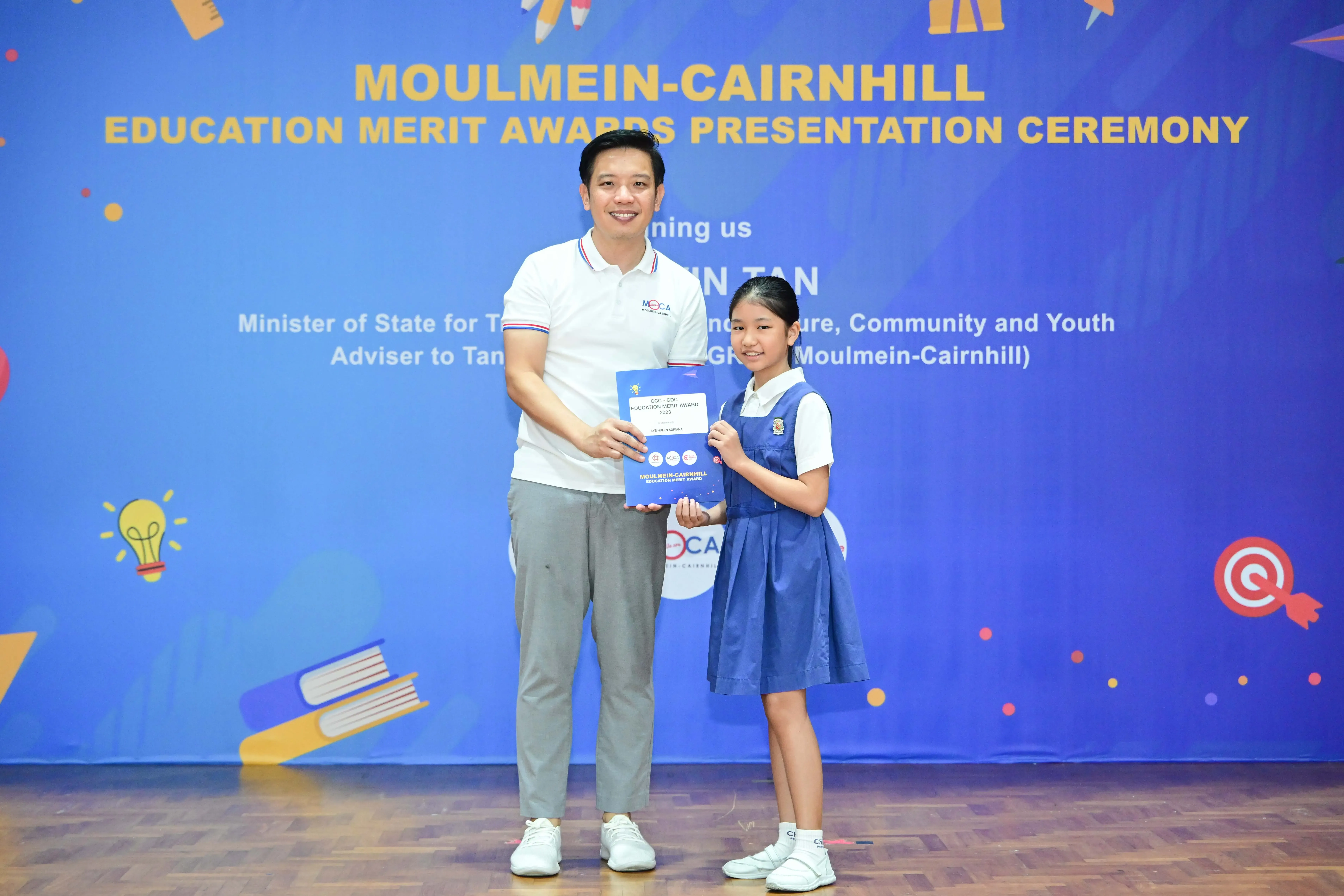 A man and a young girl in school uniform hold a certificate at the Moulmein-Cairnhill Education Merit Awards ceremony.