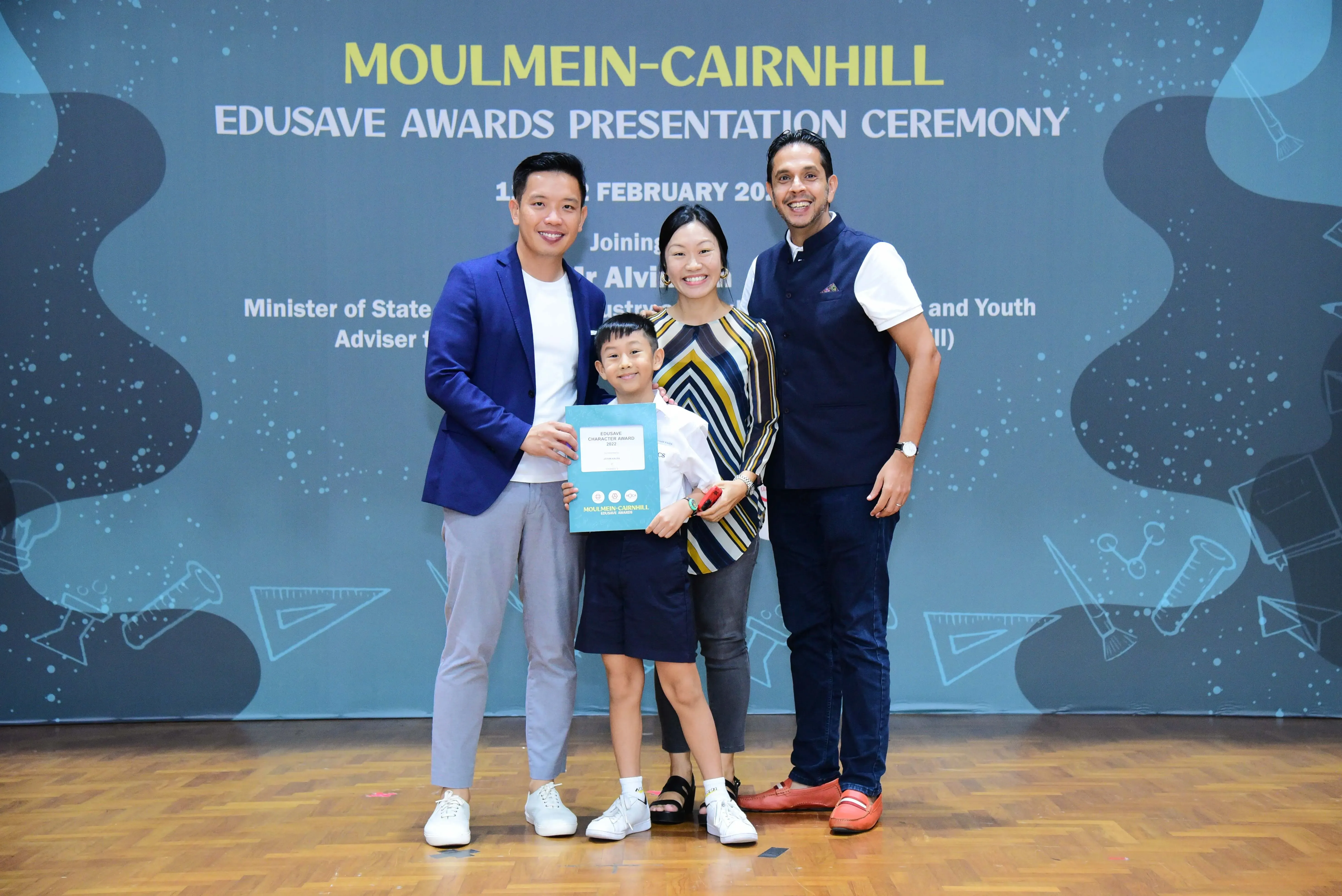 Three adults and a young boy holding a certificate pose at the Moulmein-Cairnhill Edusave Awards Presentation Ceremony.