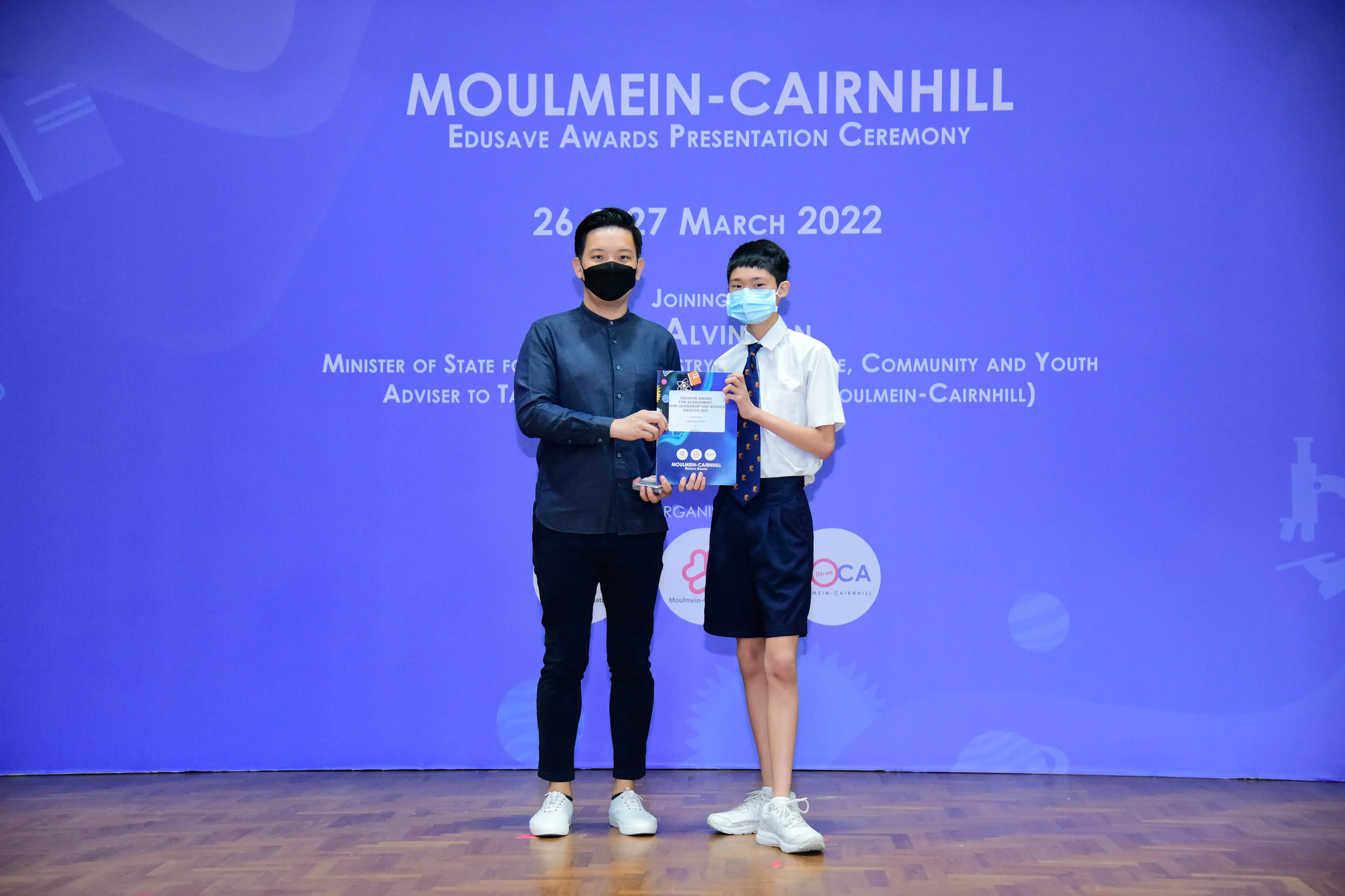 Two masked individuals hold an award certificate at the Moulmein-Cairnhill Edusave Awards Ceremony, March 2022.