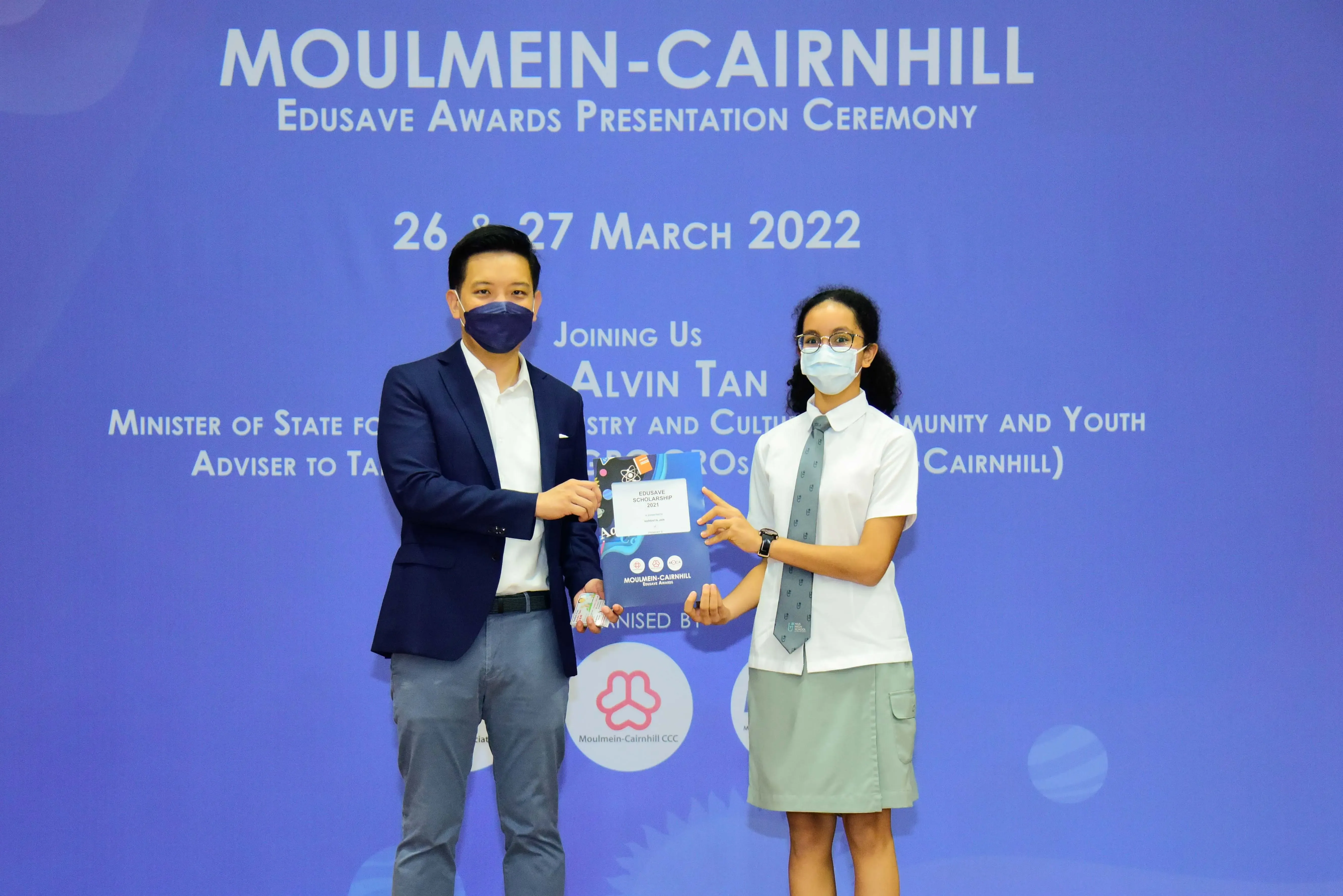 Two masked people hold an award at the Moulmein-Cairnhill Edusave Awards Presentation Ceremony, March 2022.