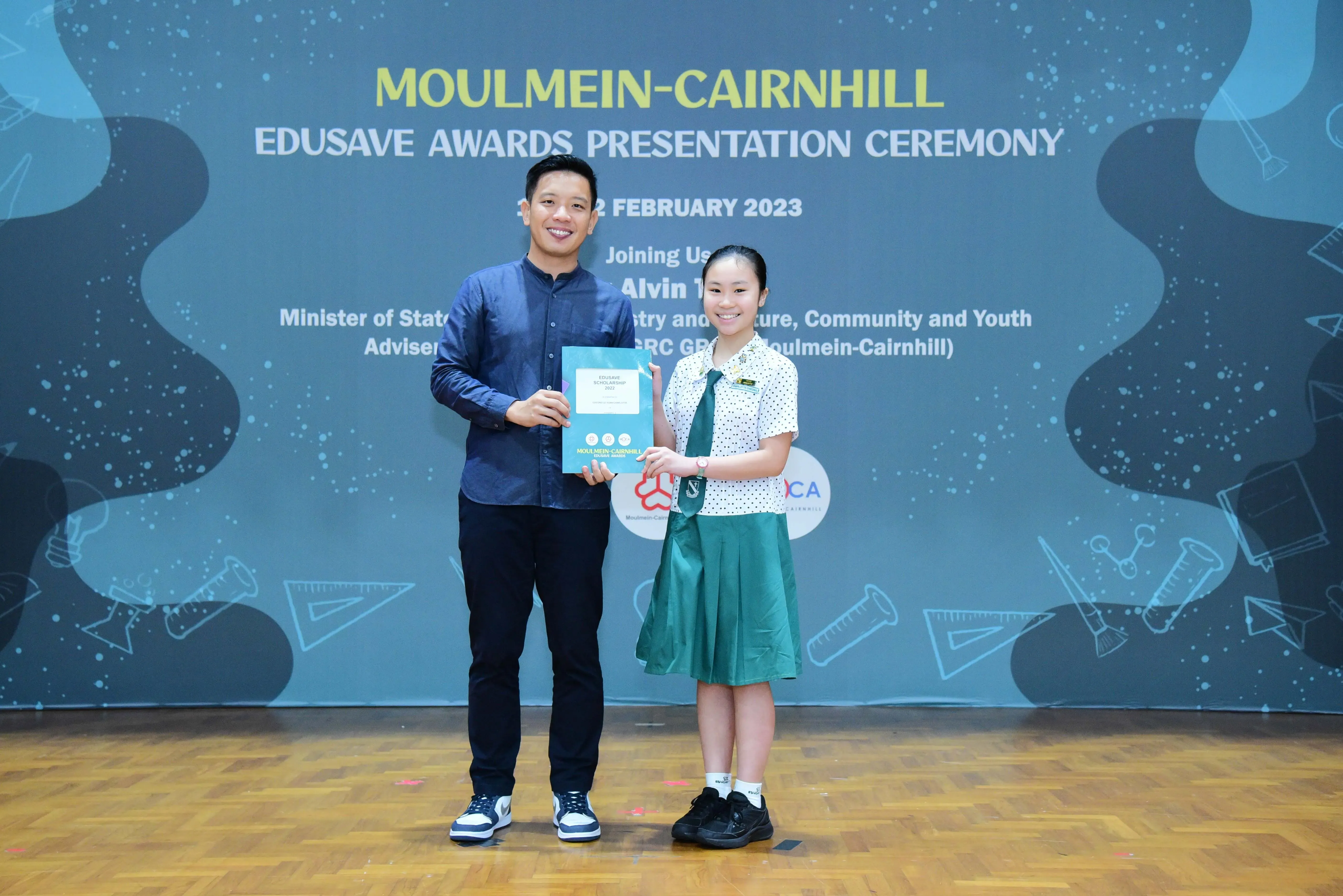 A man and a schoolgirl hold an award certificate at the Moulmein-Cairnhill Edusave Awards Ceremony, February 2023.