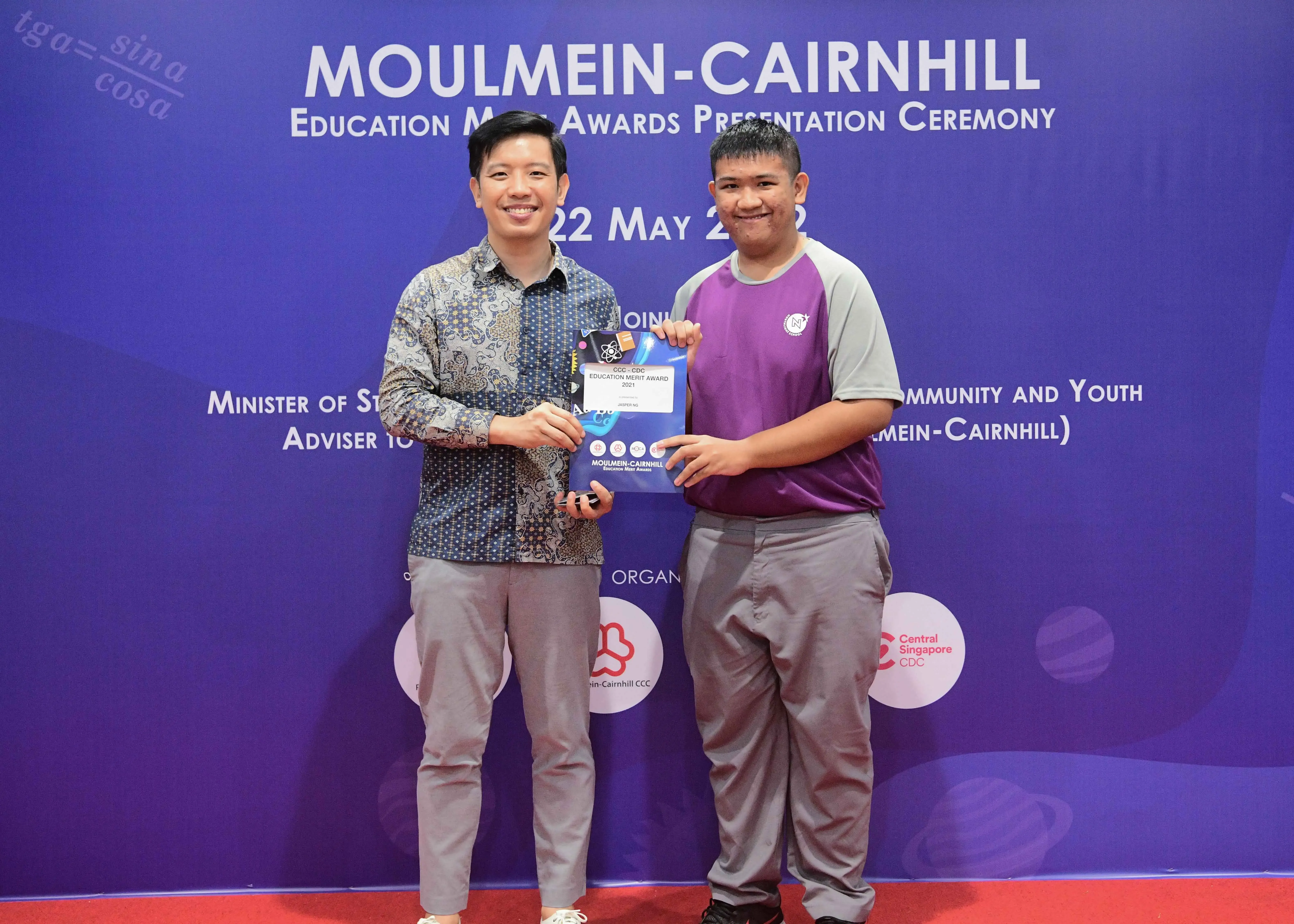 Two men smile while jointly holding an award certificate at the Moulmein-Cairnhill Education Merit Awards Ceremony.