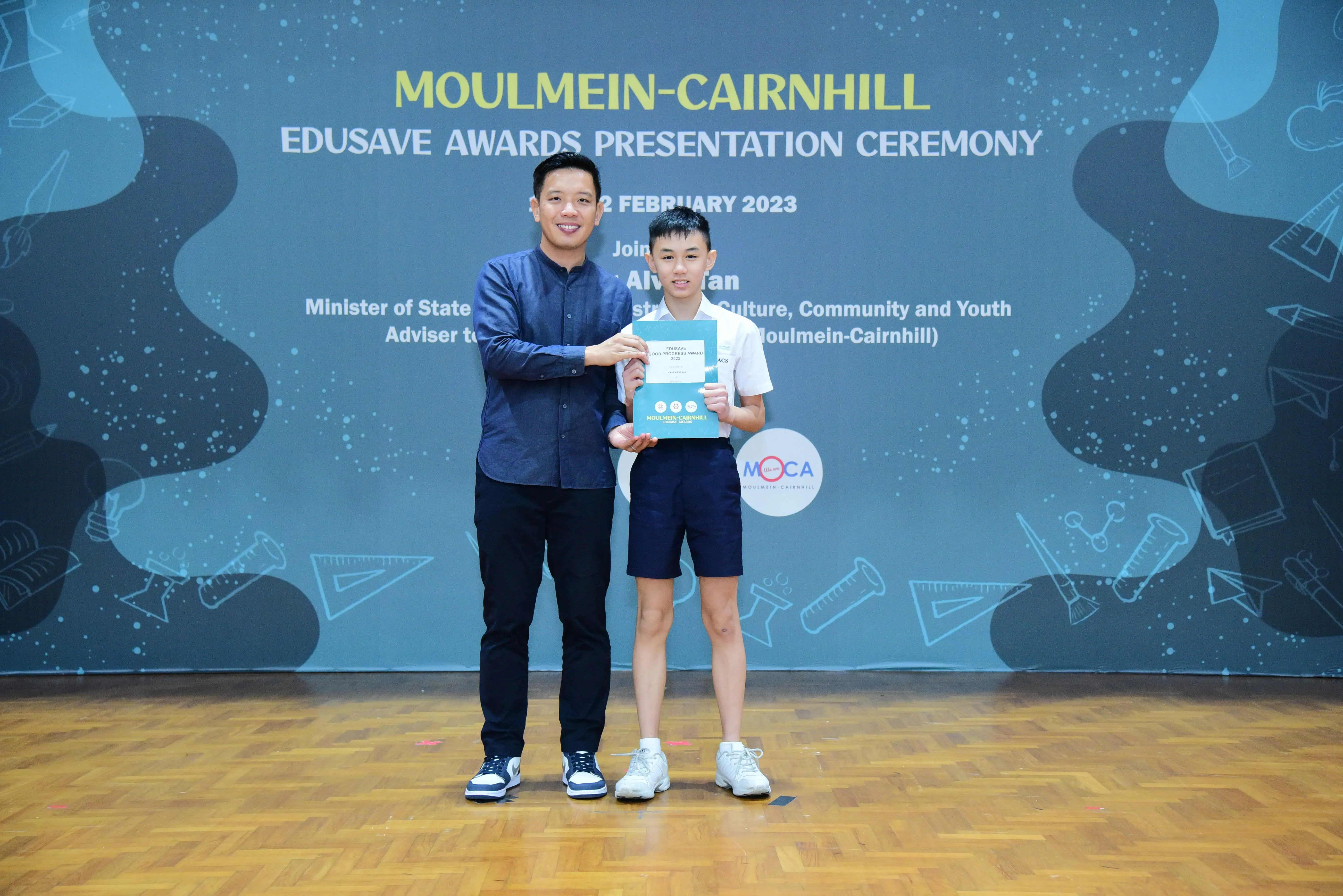 A man and a young boy hold a certificate together at the Moulmein-Cairnhill Edusave Awards Ceremony, February 2023.