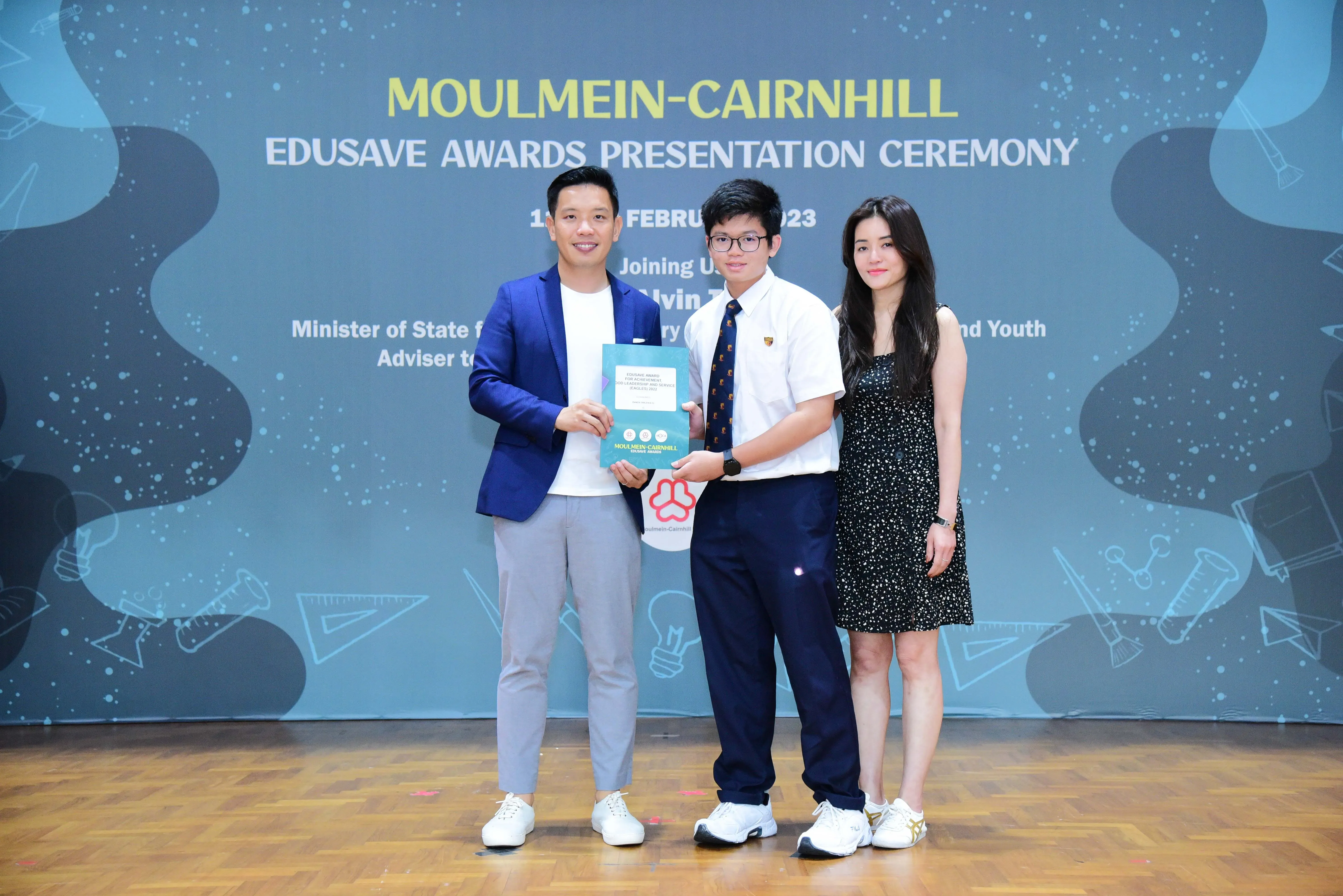 Three people pose holding a certificate at the Moulmein-Cairnhill Edusave Awards Presentation Ceremony 2023.