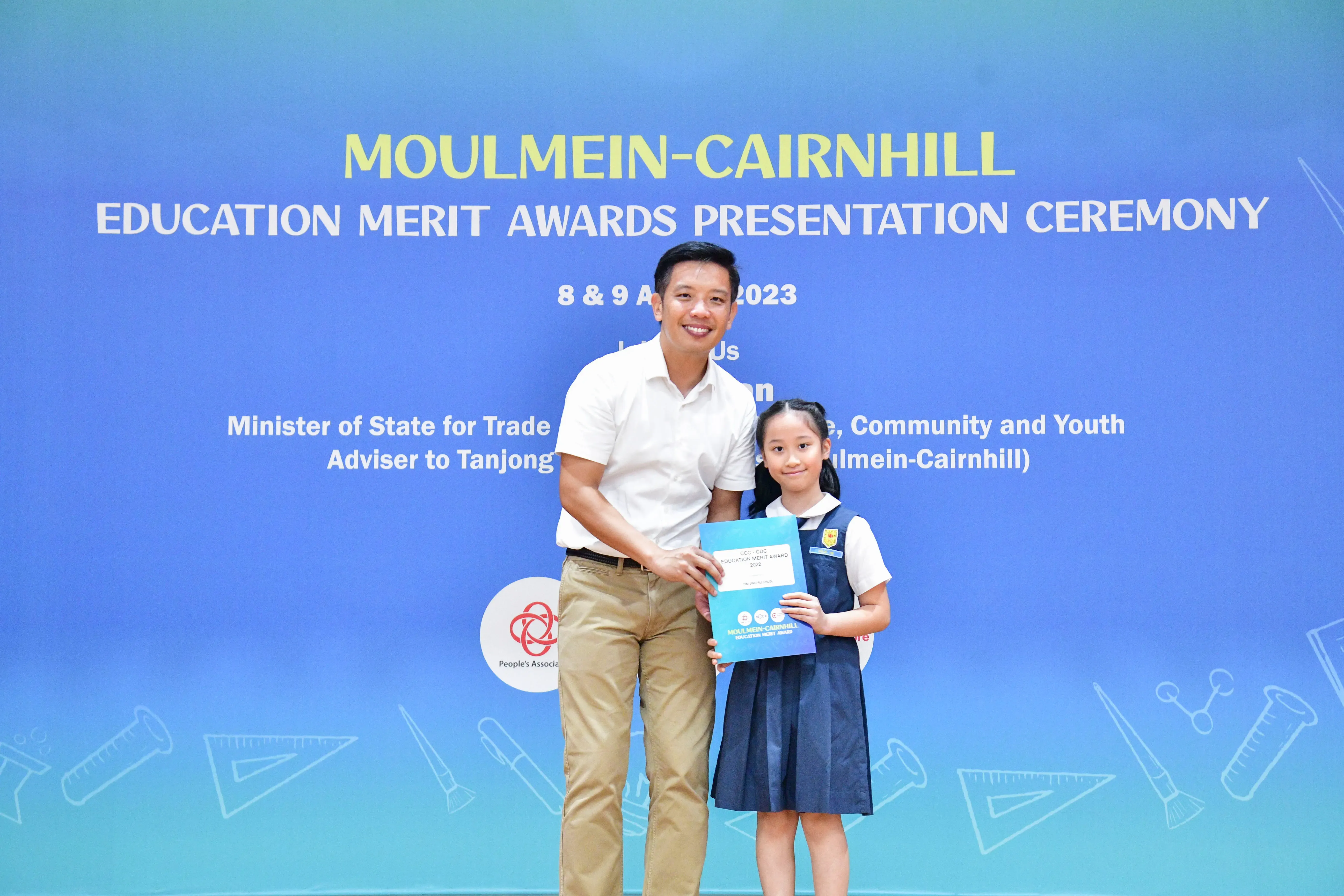 Man and young girl hold an award certificate at the Moulmein-Cairnhill Education Merit Awards Ceremony 2023.
