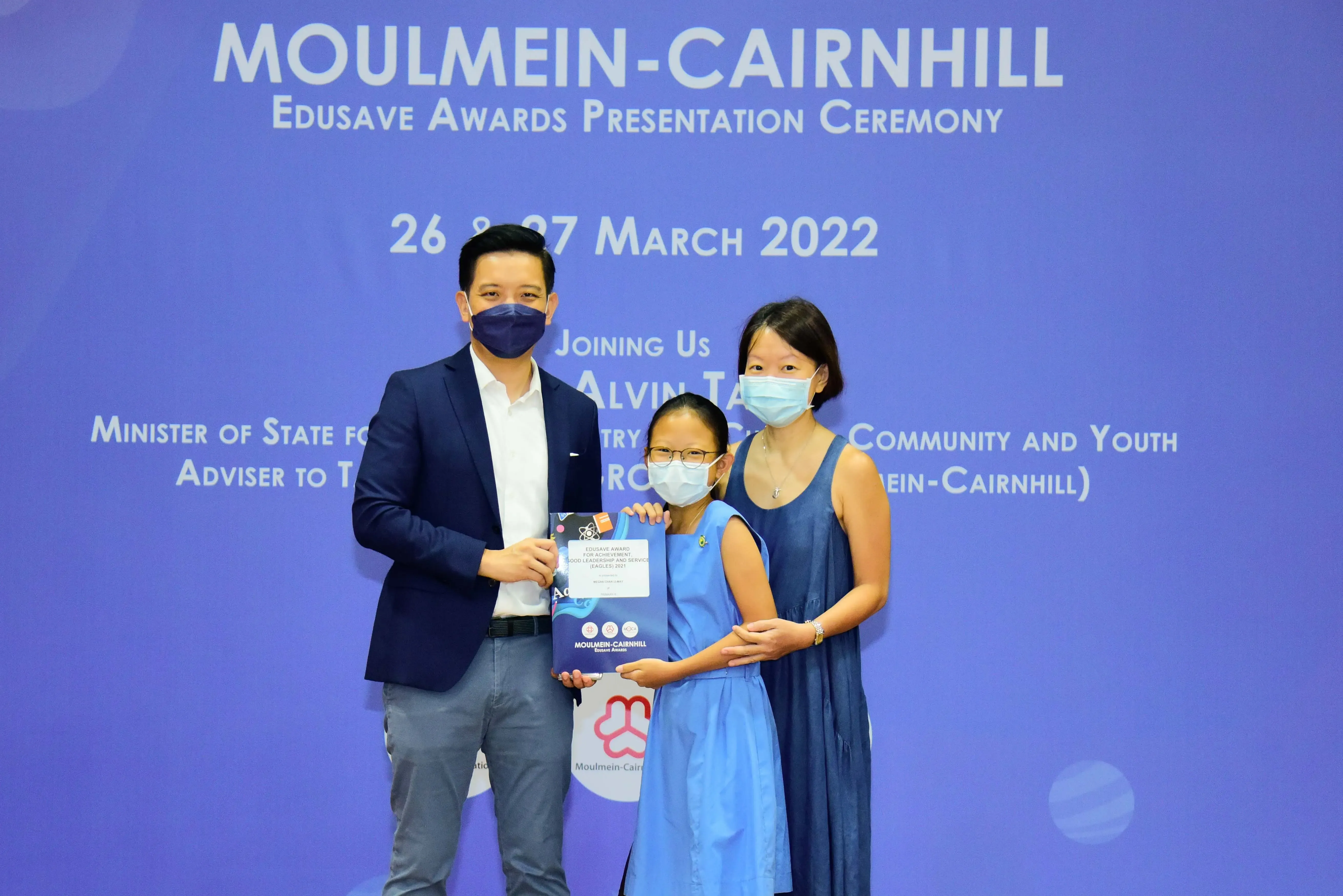 Three masked people pose with an award at the Moulmein-Cairnhill Edusave Awards Ceremony, March 2022.