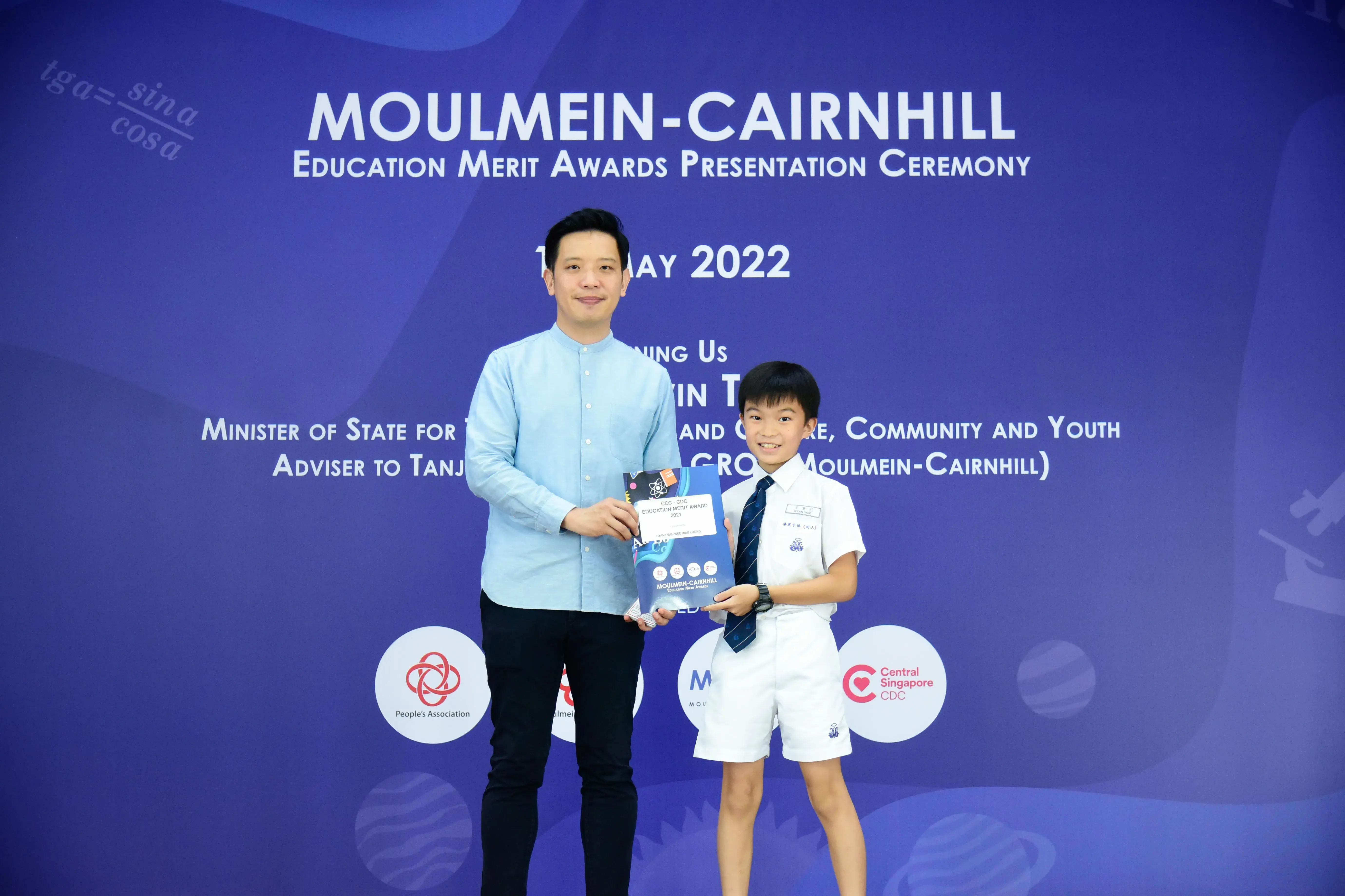 An adult and a young boy in school uniform hold an award at the Moulmein-Cairnhill Education Merit Awards 2022.