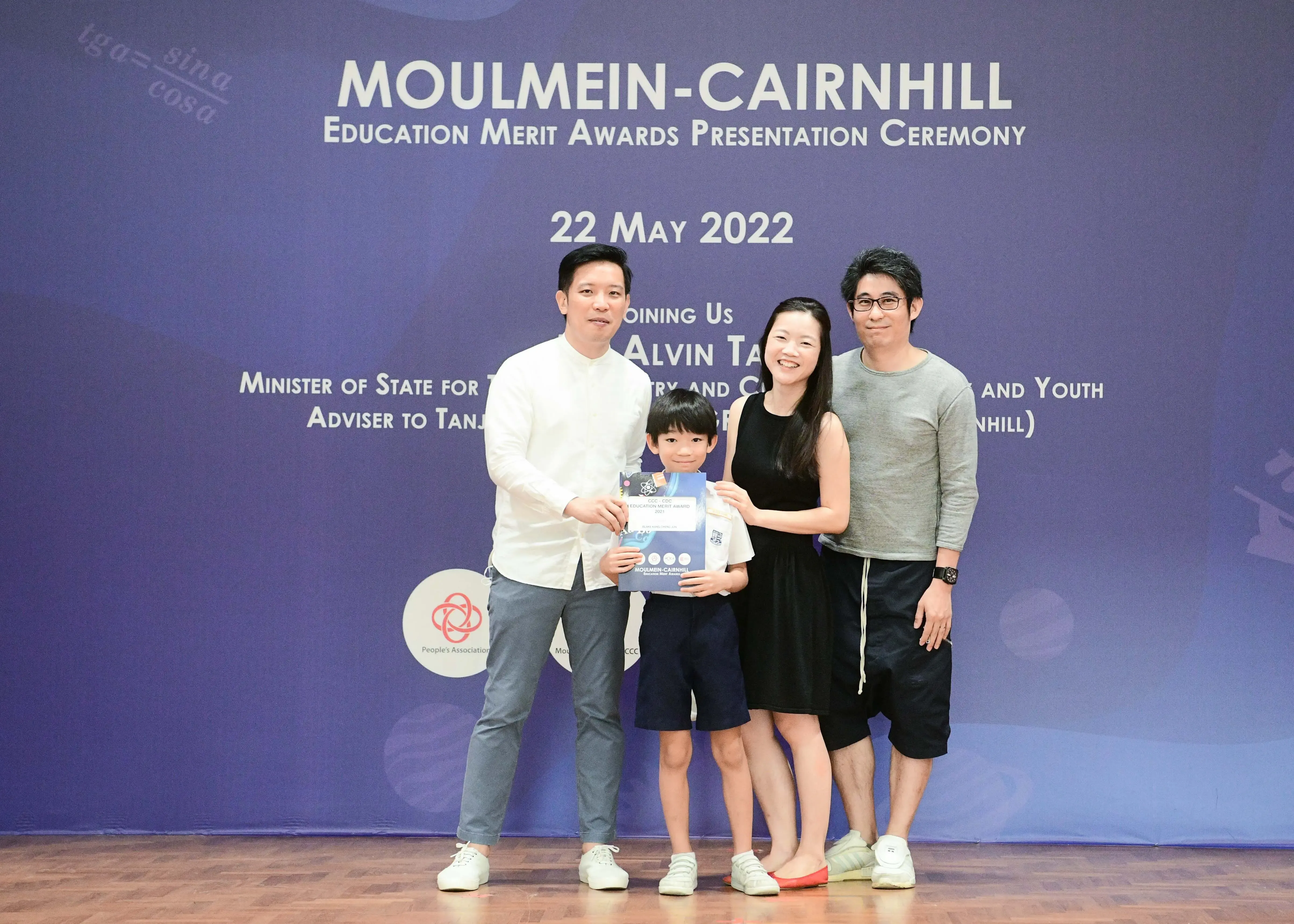 Three adults and a young boy pose with a certificate at the Moulmein-Cairnhill Education Merit Awards, May 2022.