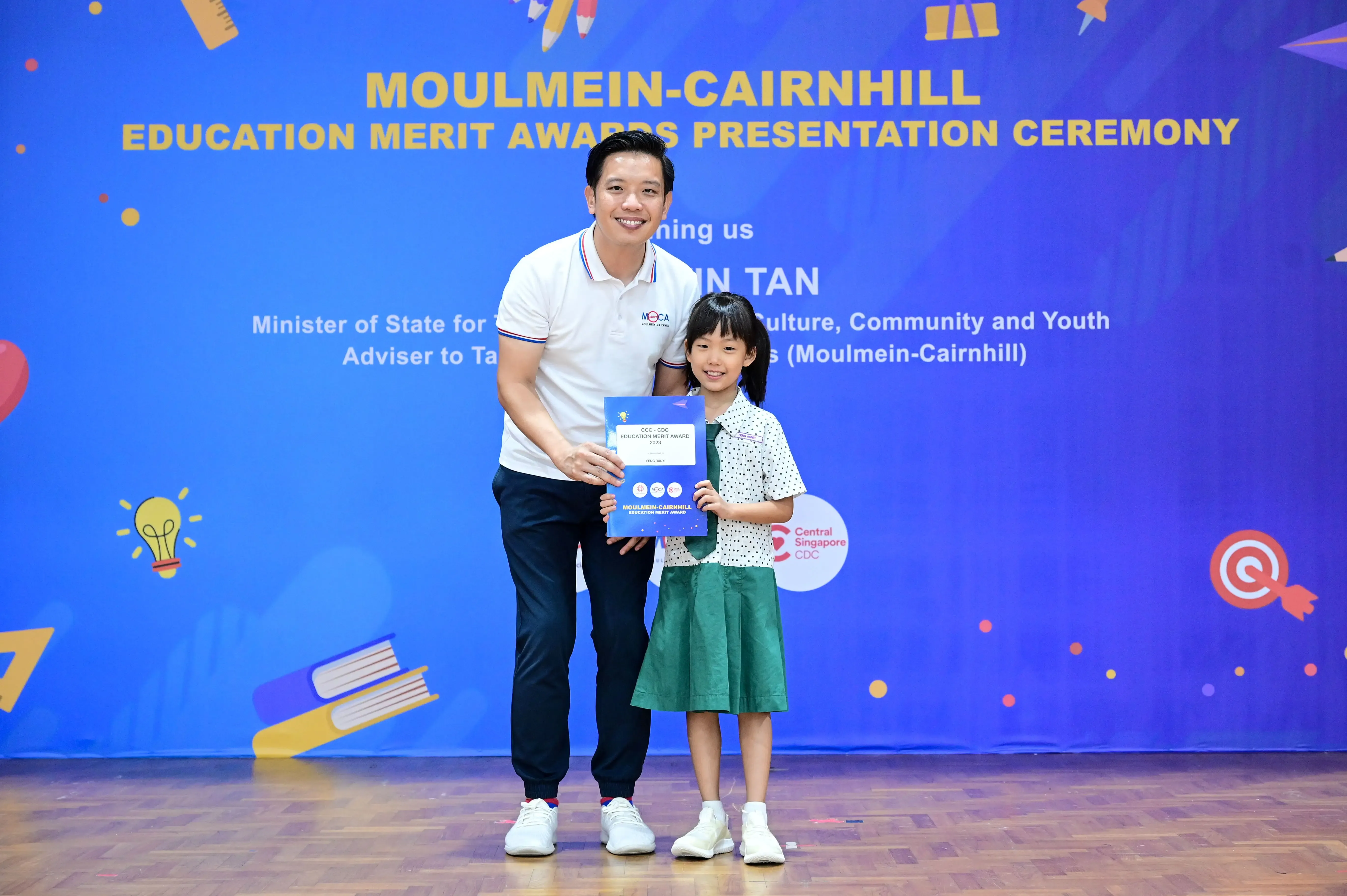 A man and a young girl holding a certificate at the Moulmein-Cairnhill Education Merit Awards Presentation Ceremony.