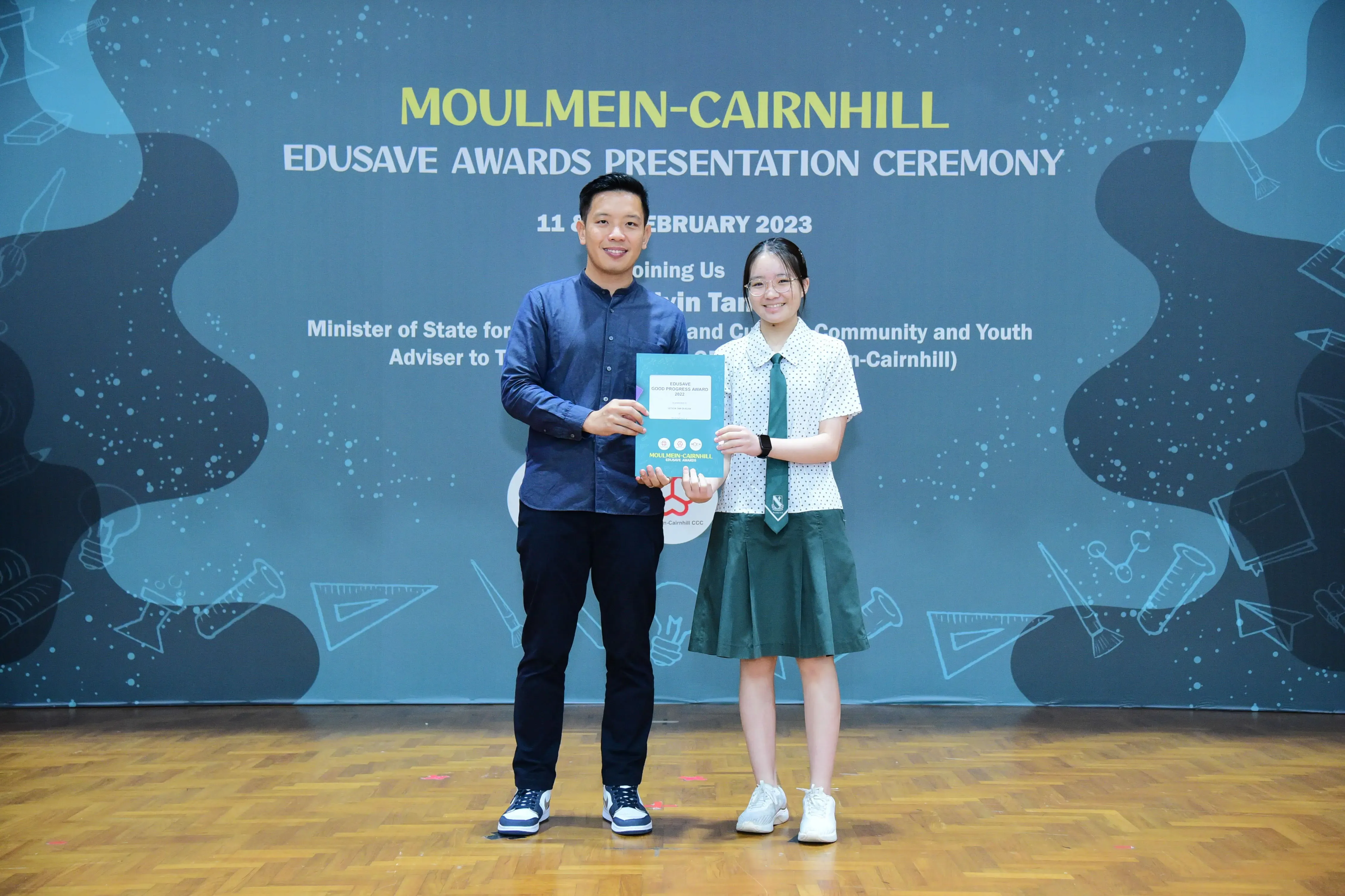 A man and a young girl in school uniform hold a certificate at the Moulmein-Cairnhill Edusave Awards Ceremony 2023.