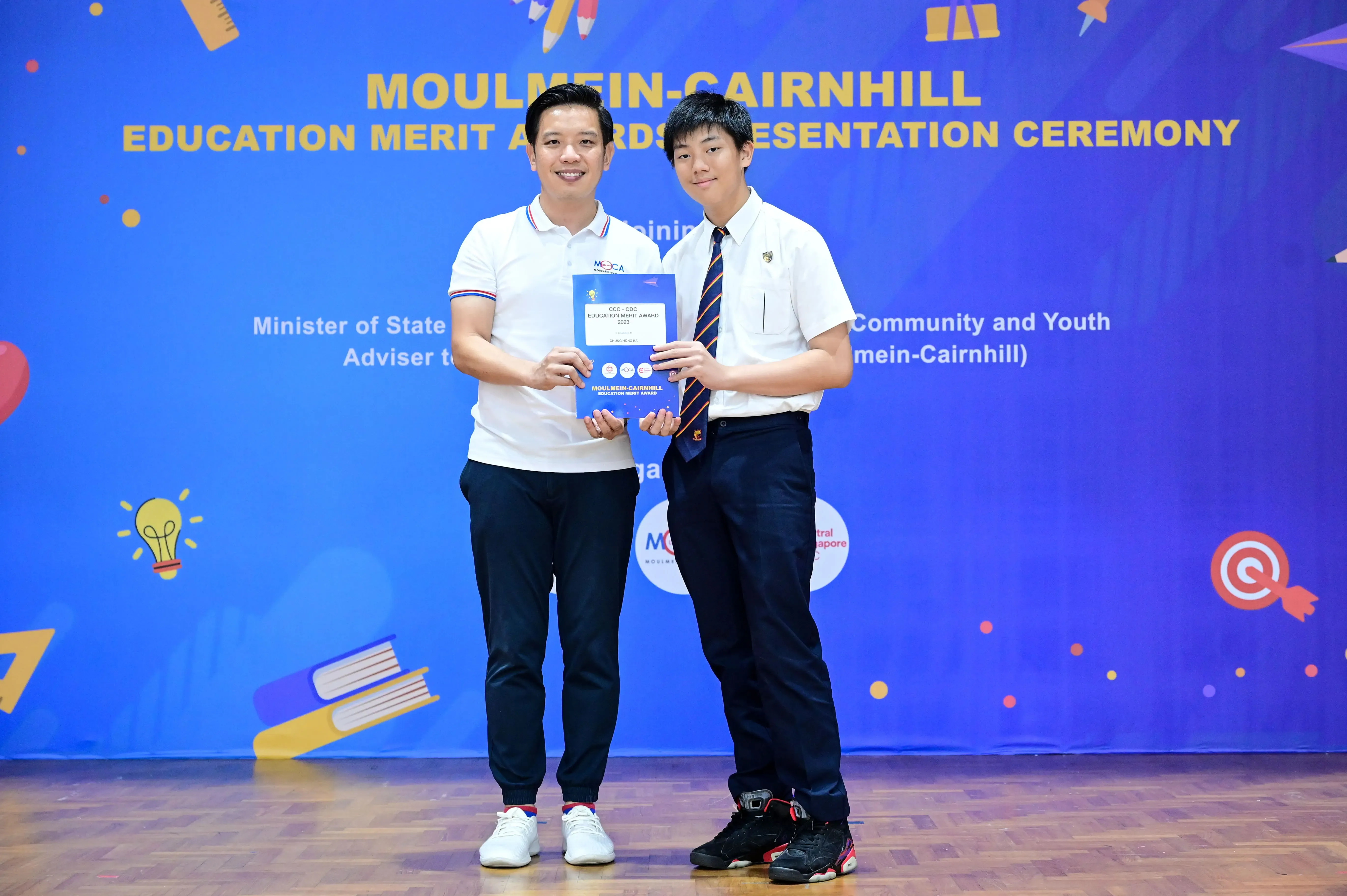 Two men hold an award certificate together at the Moulmein-Cairnhill Education Merit Awards Presentation Ceremony.