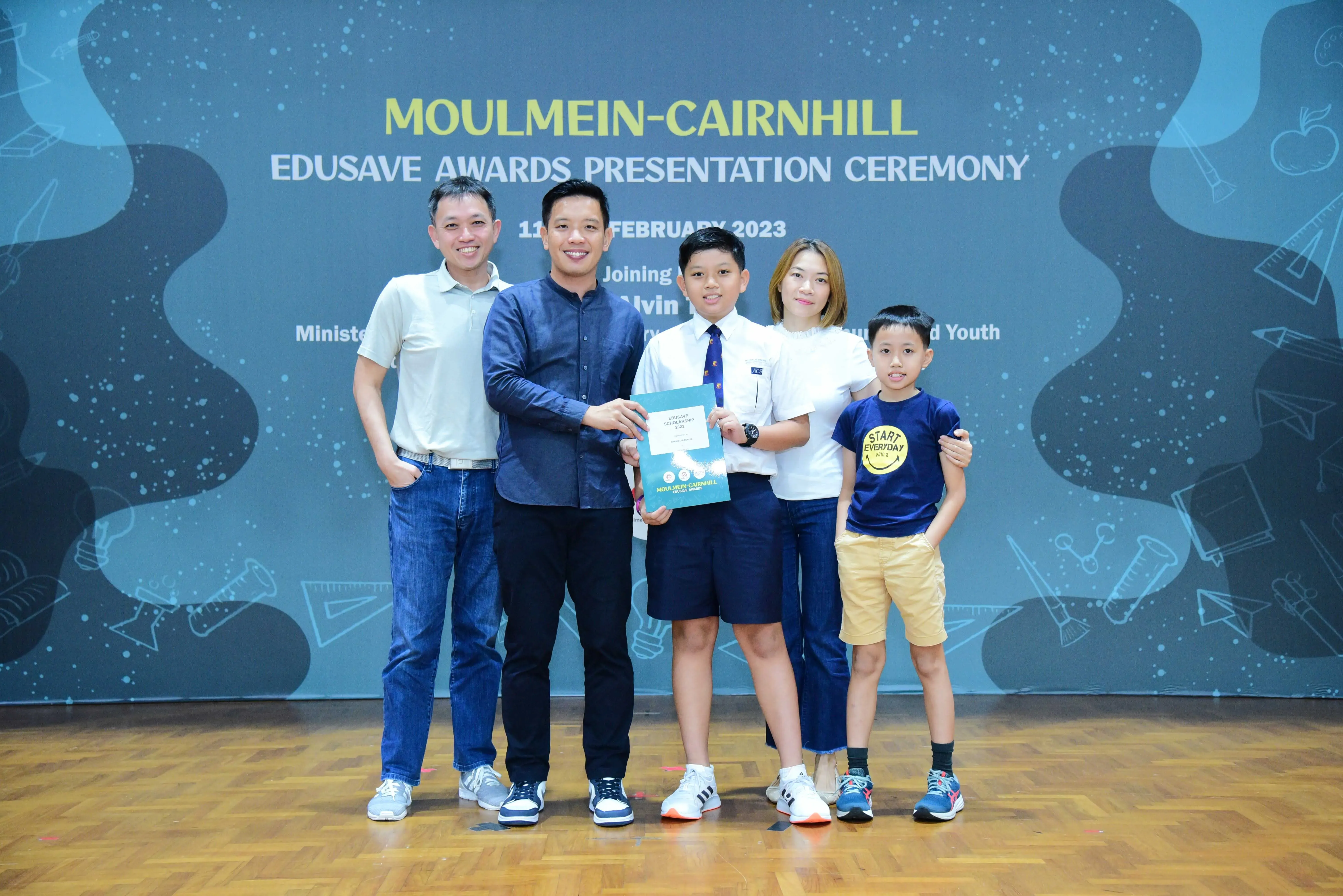 Five people pose at the Moulmein-Cairnhill Edusave Awards Presentation Ceremony, with a boy holding a certificate.